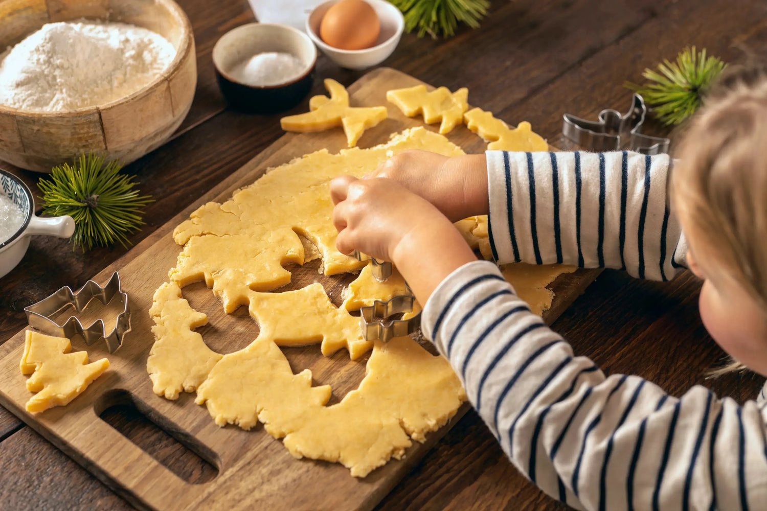 Child making Christmas cookies with tree-shaped cutters on wooden table