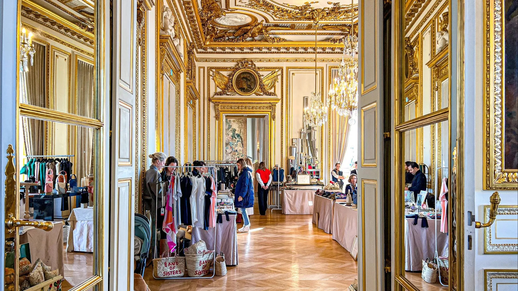 Luxury boutique pop-up inside ornate gold-accented room with chandeliers and designer clothing racks