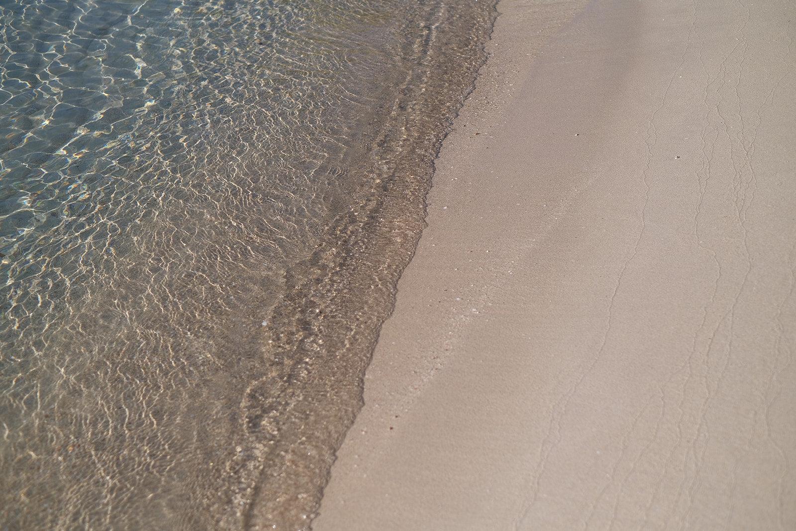 Clear water meeting sandy beach shoreline under sunlight
