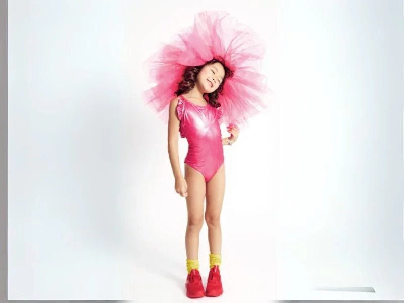 Girl wearing metallic pink one-piece swimsuit, pink tulle headpiece, yellow socks, red shoes