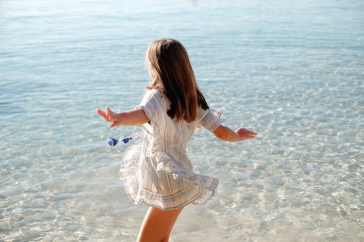 Girl in a striped beach caftan enjoying clear shallow water at the seaside