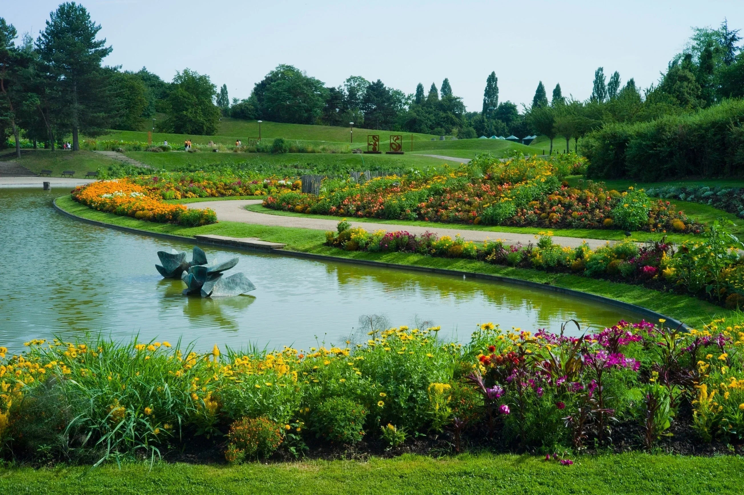 Colorful flower garden with pond, modern sculpture, and lush green park landscaping