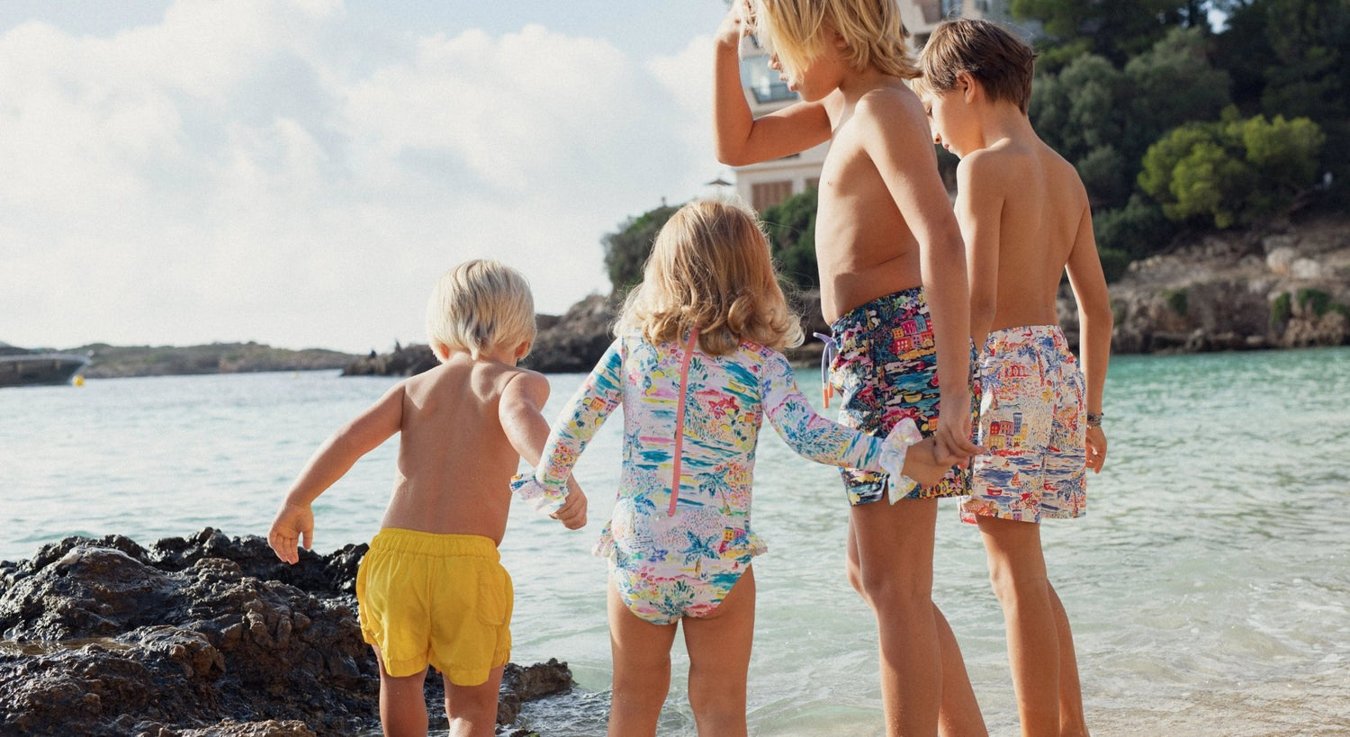 Children in colorful UV swimwear and beach shorts standing on a sunny beach by the water