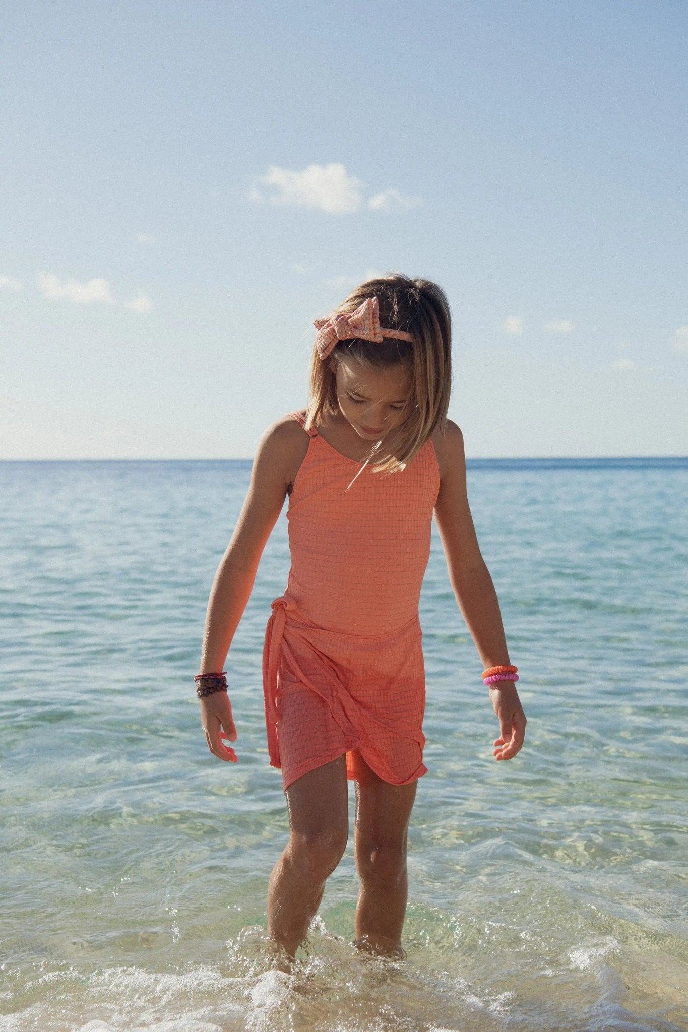 Girl in coral UV-protective swimsuit and wrap skirt playing at the seaside on a sunny day