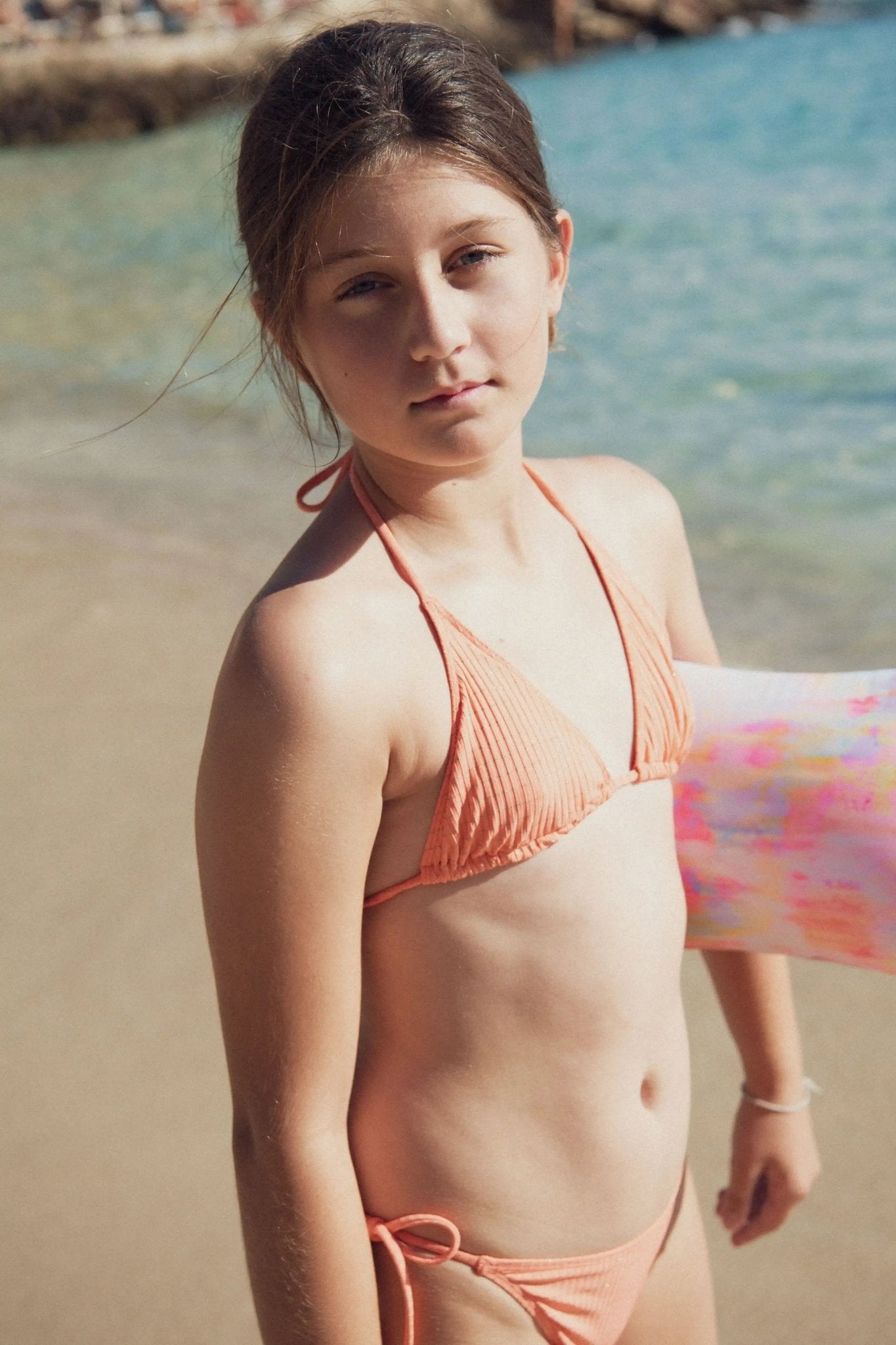 Girl in coral bikini on beach with inflatable pool float and ocean background