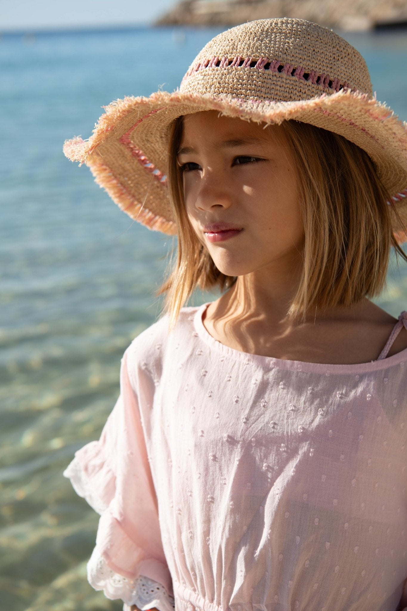 Girl in a pink sun hat and light pink summer dress by the seaside