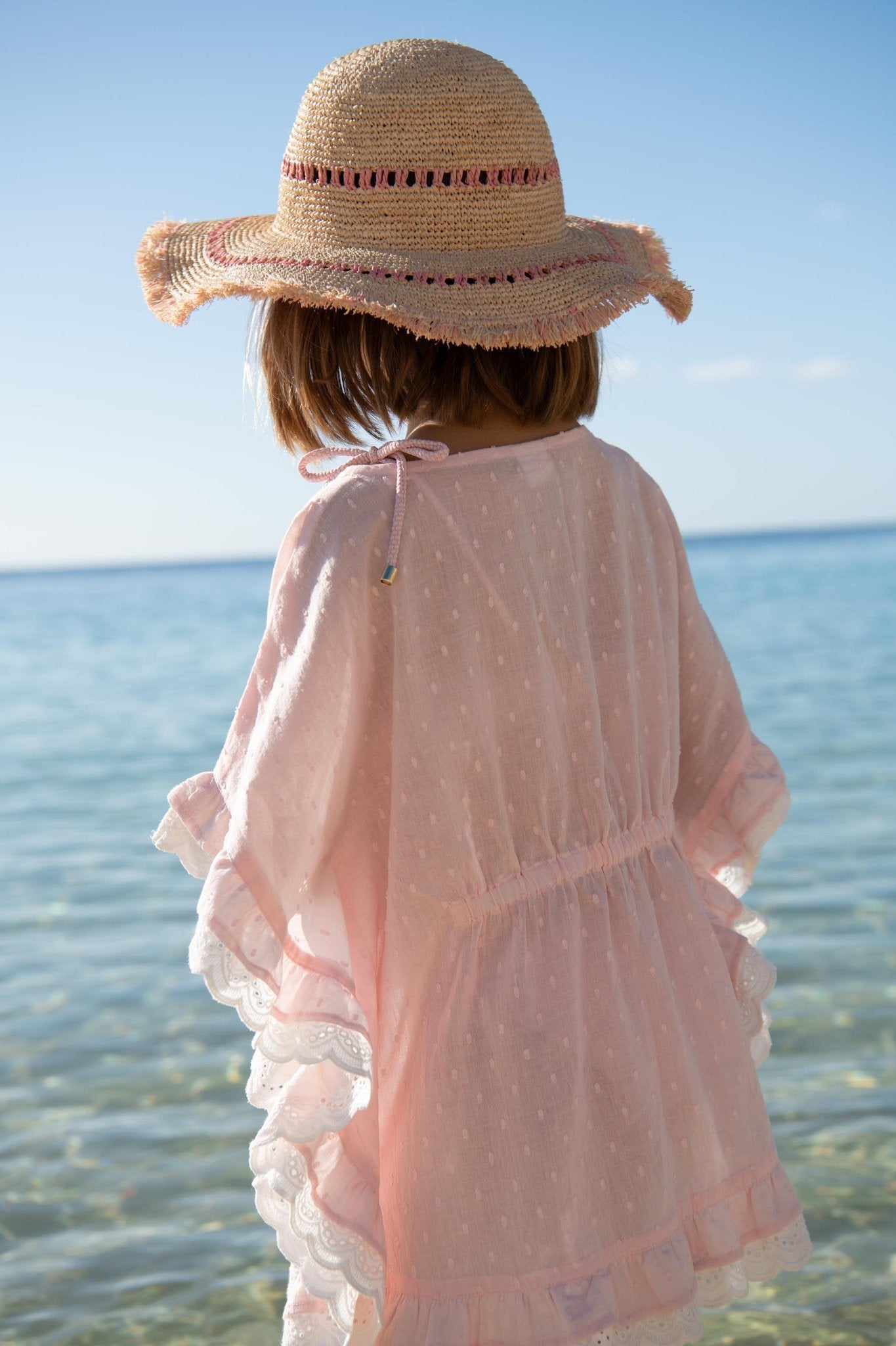 Girl in pink beach cover-up and straw sun hat by the sea