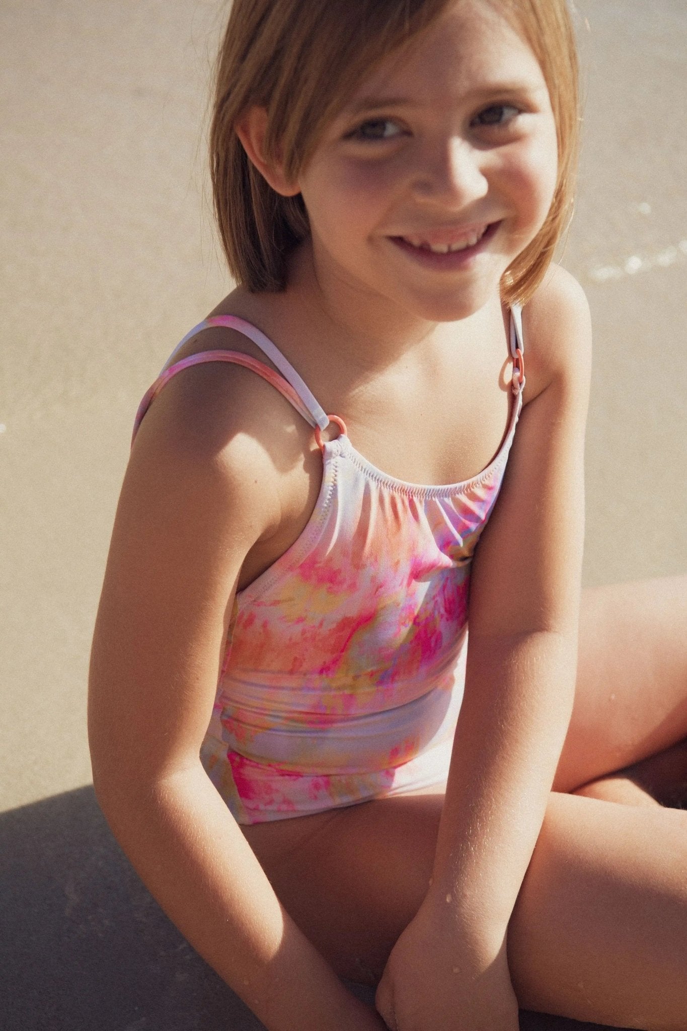 Smiling girl at the beach in a colorful one-piece swimsuit with pink and orange patterns