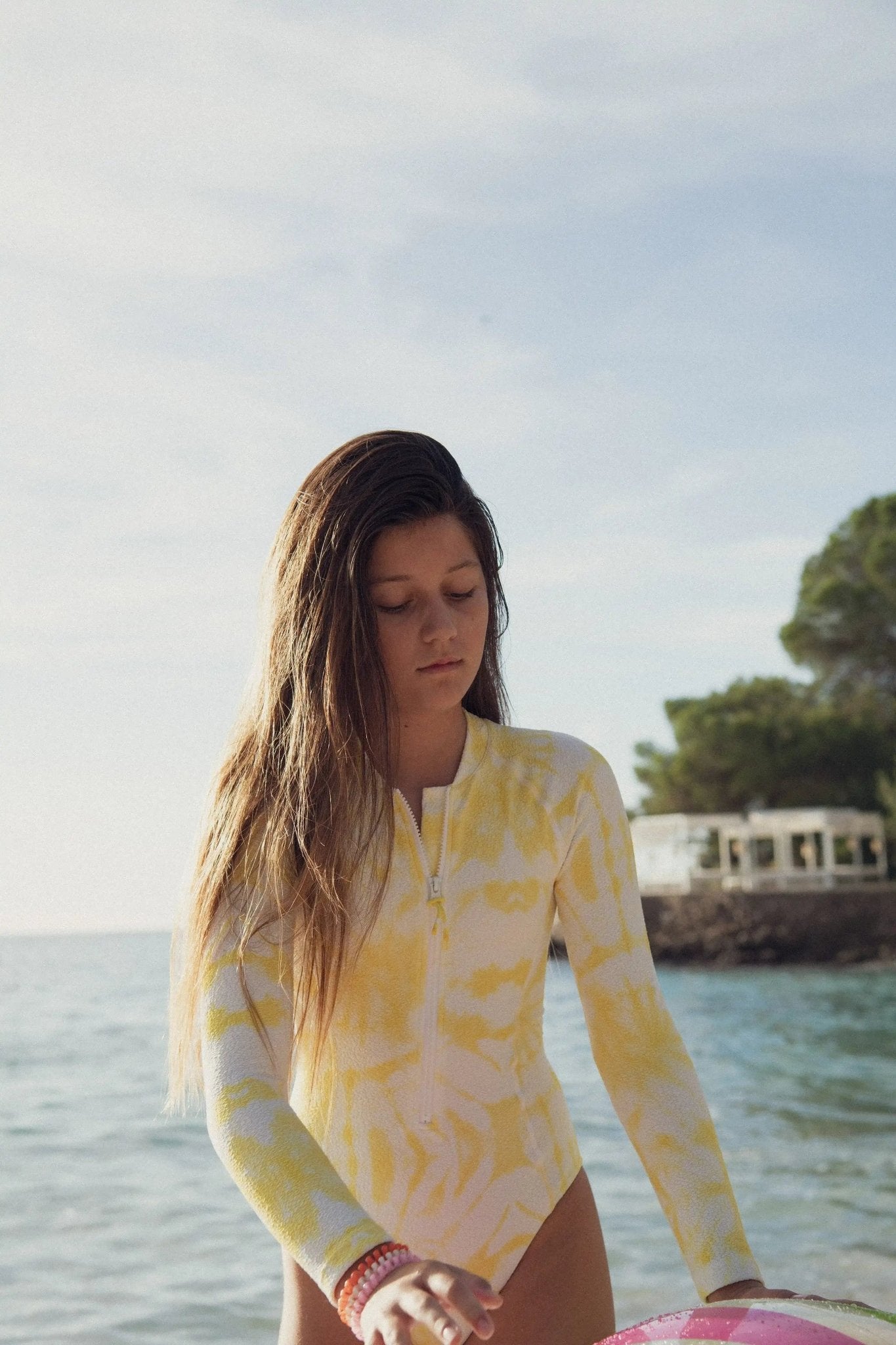 Girl in yellow long-sleeve UV swimwear standing by the sea on a sunny beach