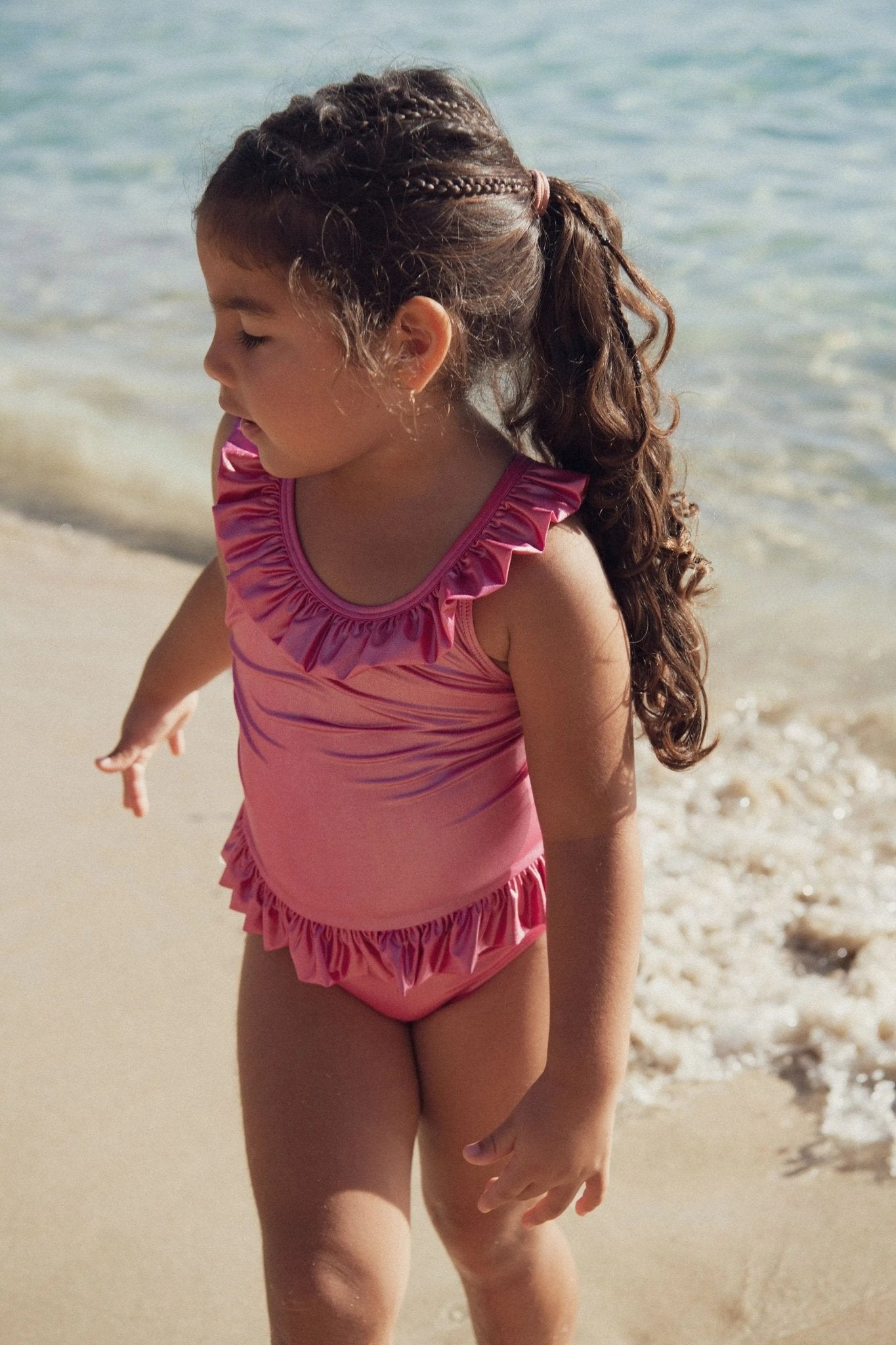Girl in pink ruffled swimsuit walking on the beach near the water