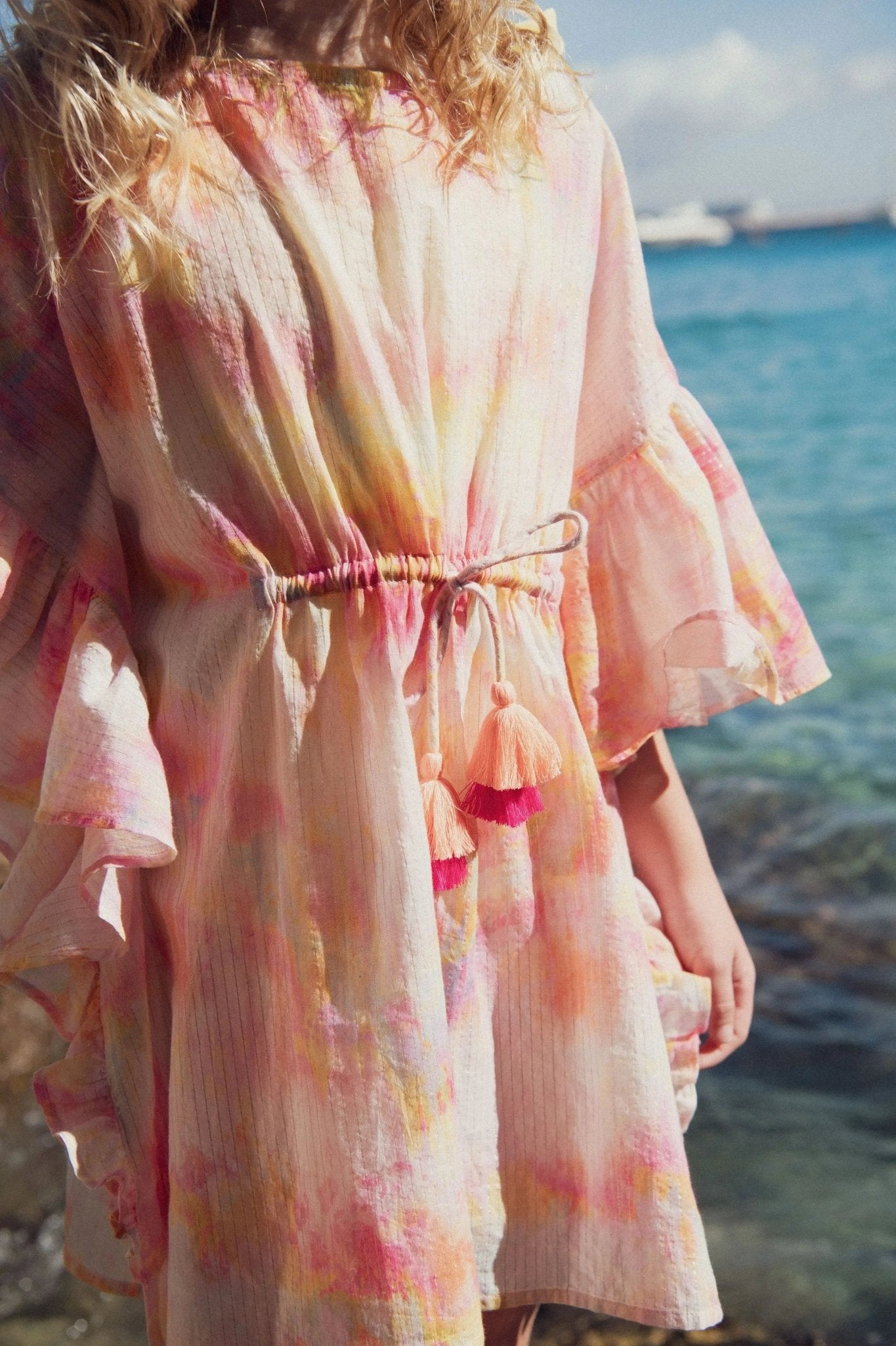 Girl wearing pastel tie-dye beach dress with tassels by the seaside
