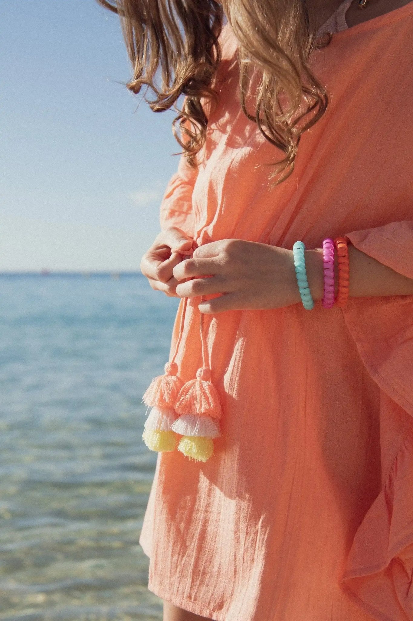 Girl in a peach beach cover-up with tassels and colorful bracelets by the sea