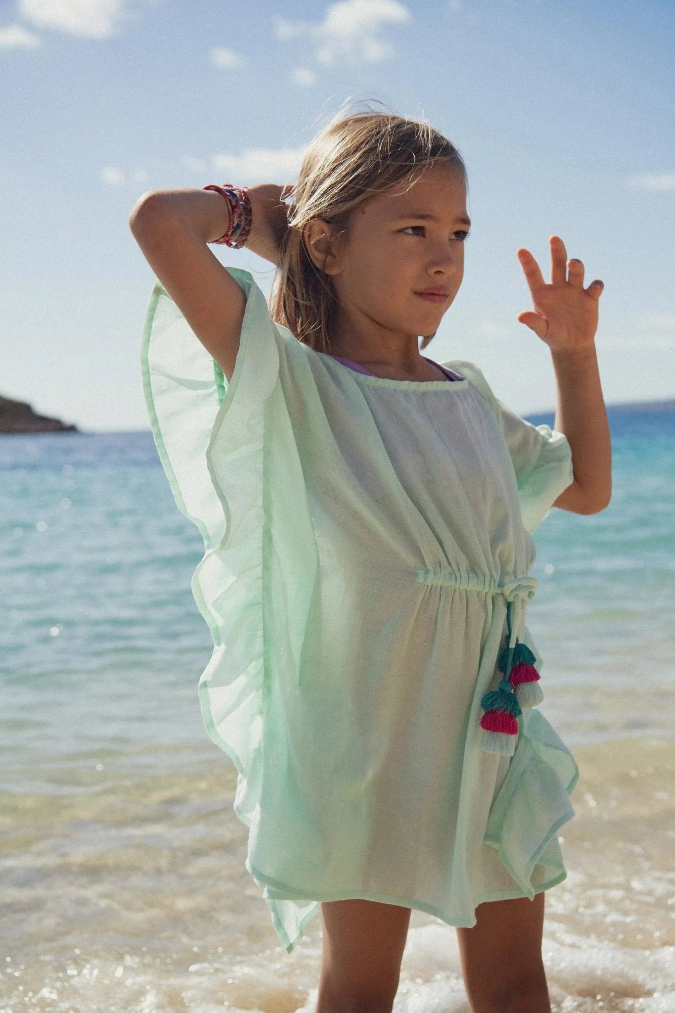 Girl wearing light aqua beach cover-up dress with tassels by the sea