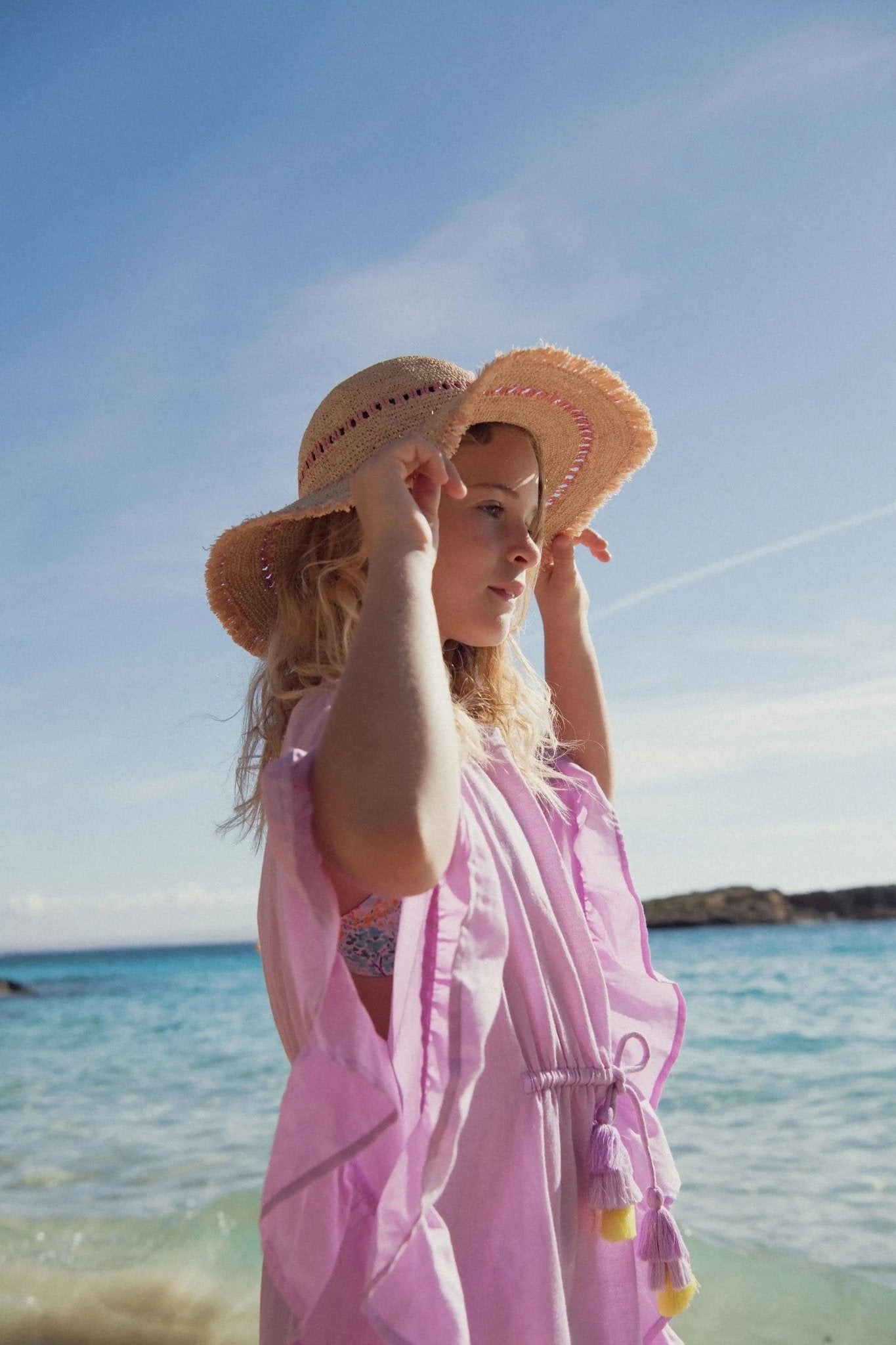 Girl in lilac beach dress and straw hat standing by the seaside on a sunny day