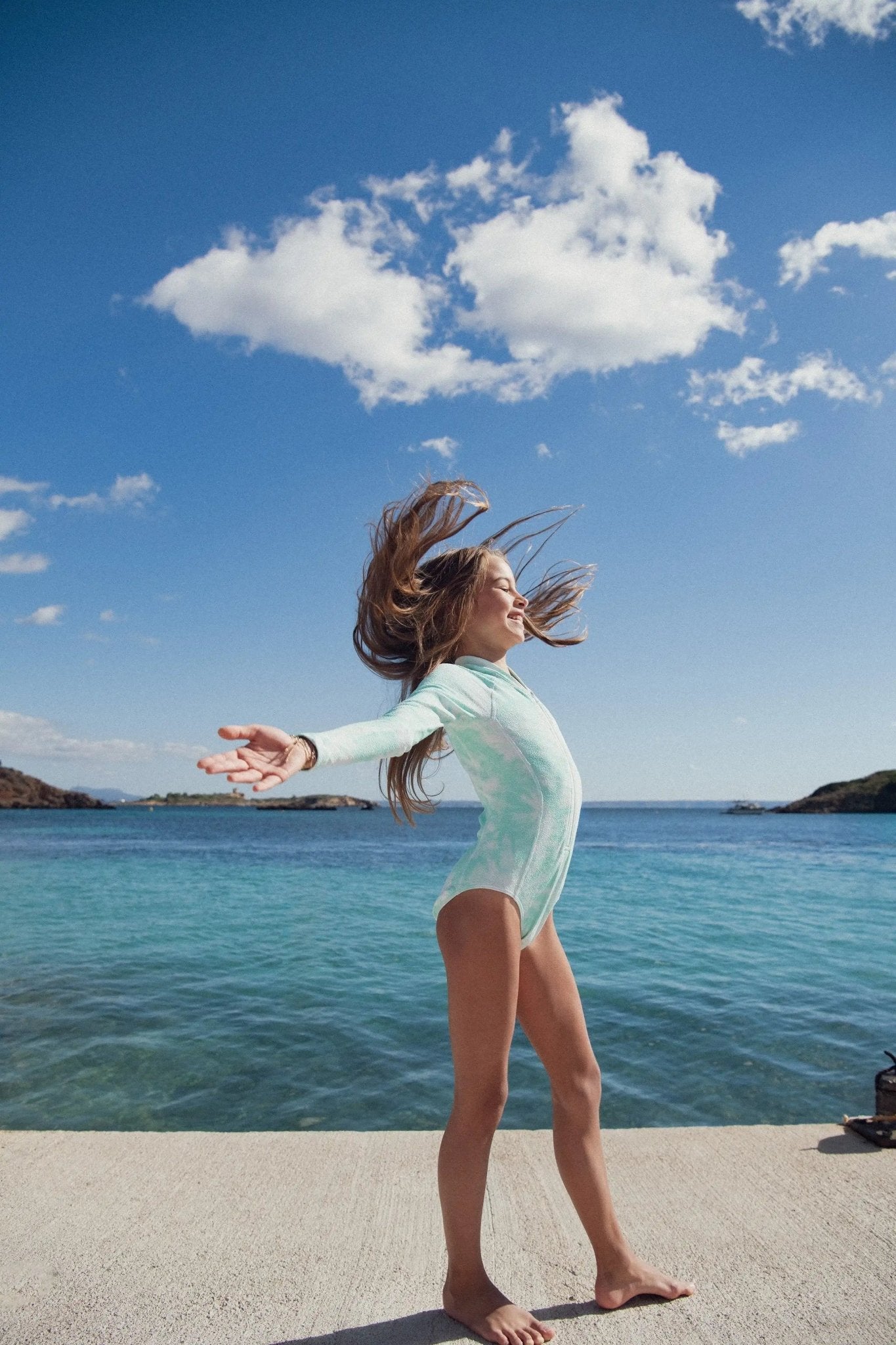 Girl in long-sleeve UV swimsuit enjoying beach, blue sea and sky in the background