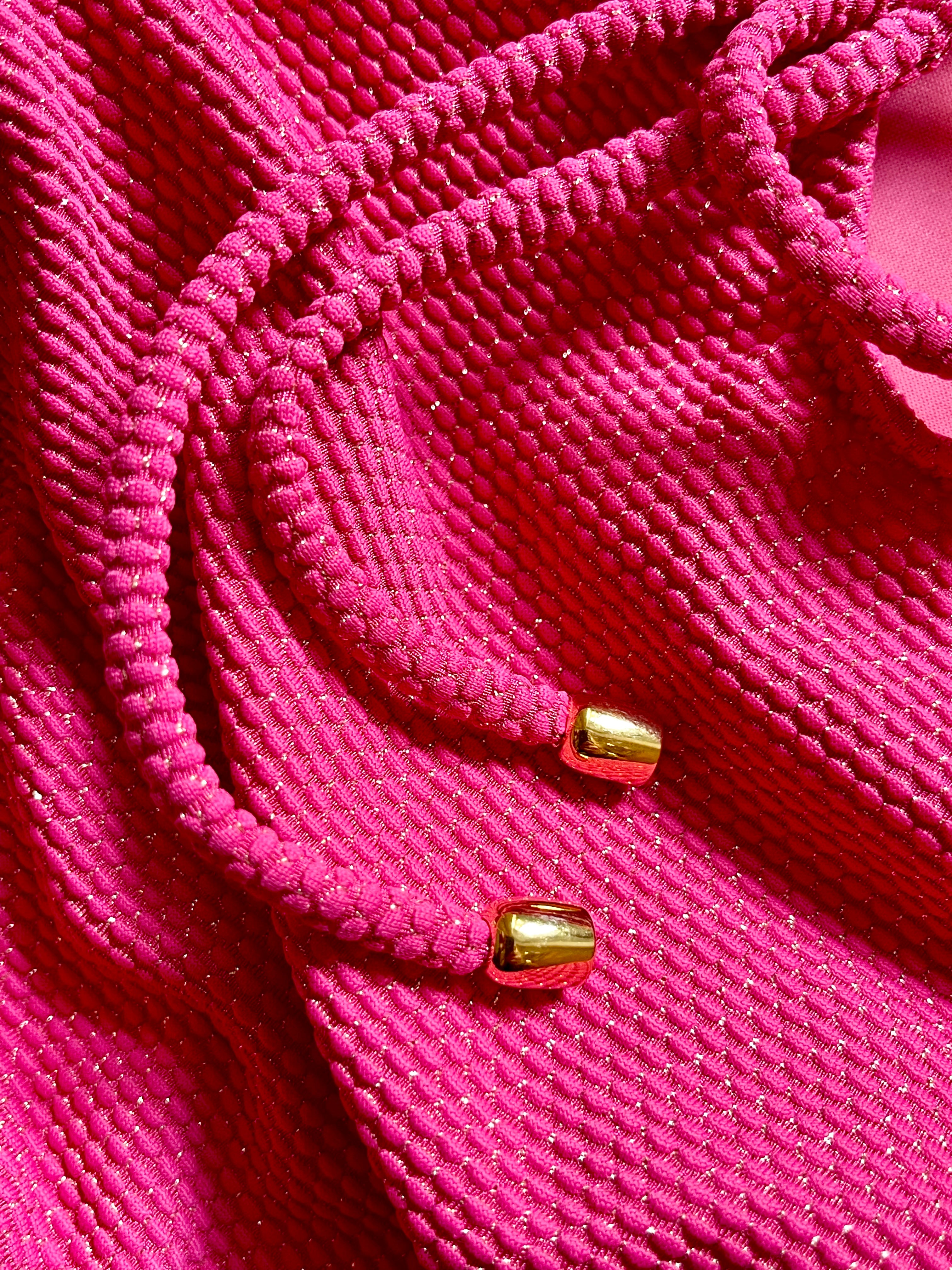 Close-up of raspberry pink textured bikini fabric with braided straps and gold metal tips