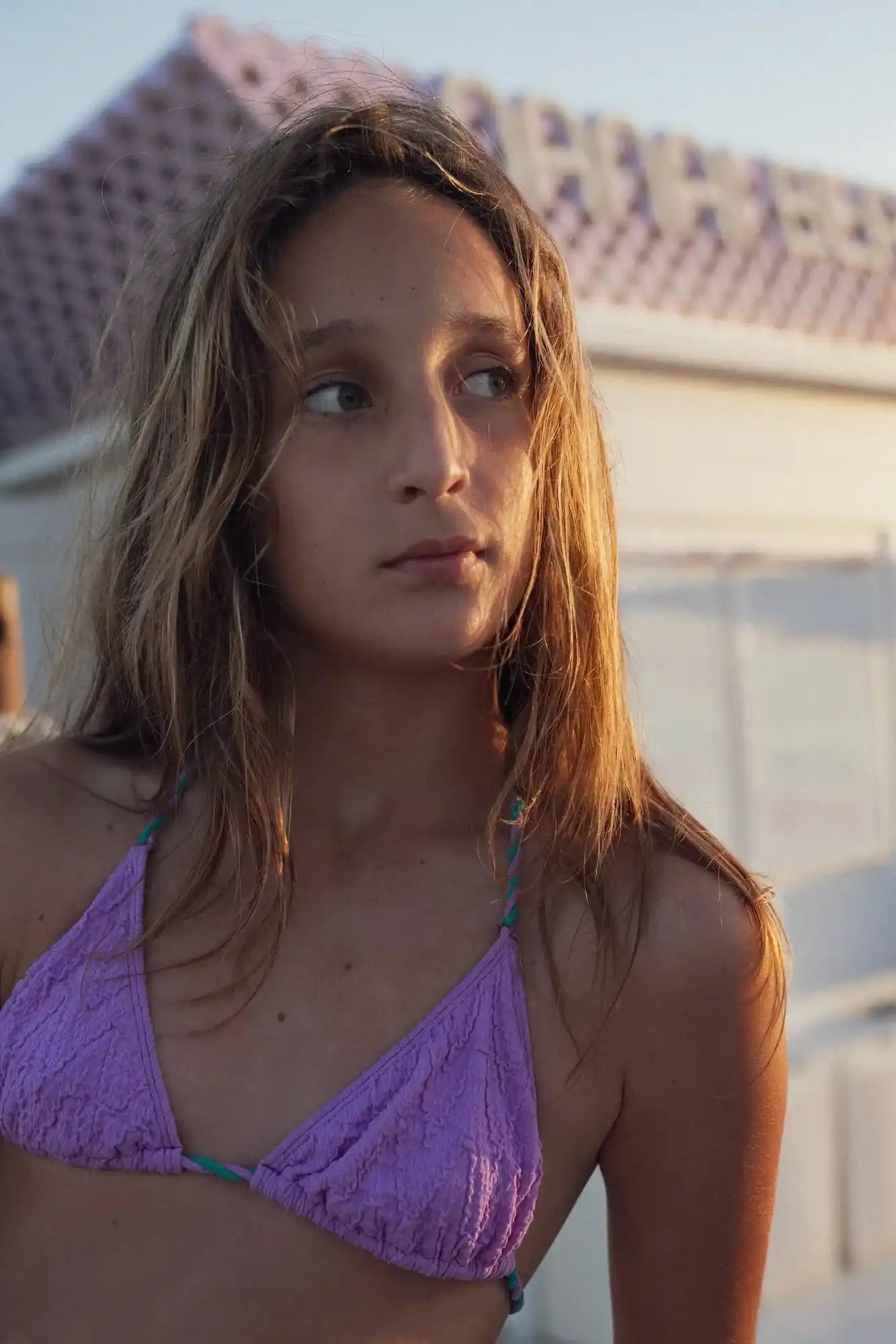 Girl wearing a violet triangle bikini top from Lison Paris, outdoors in soft sunlight