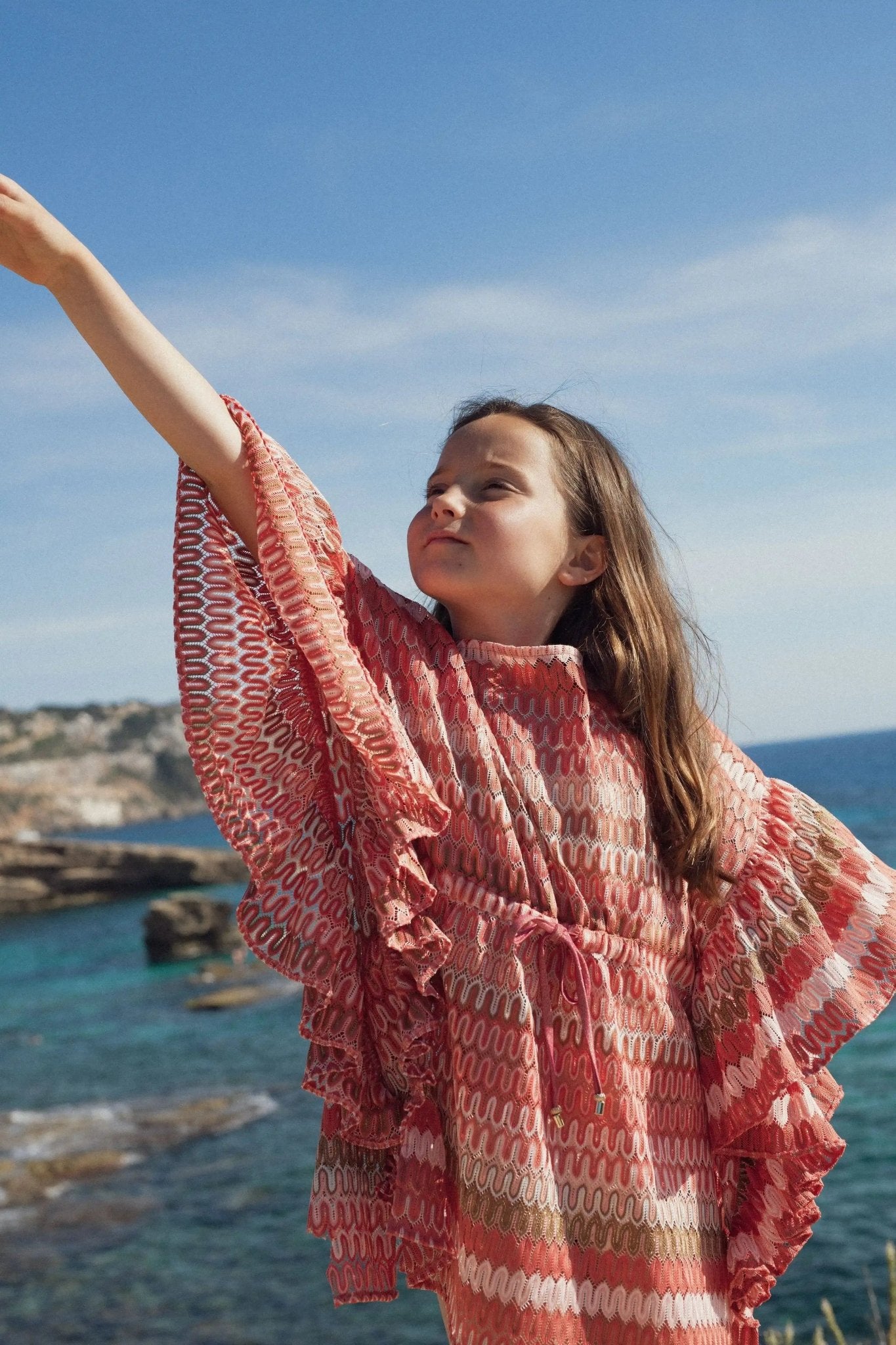 Girl in coral crochet beach caftan with ruffle sleeves by the sea