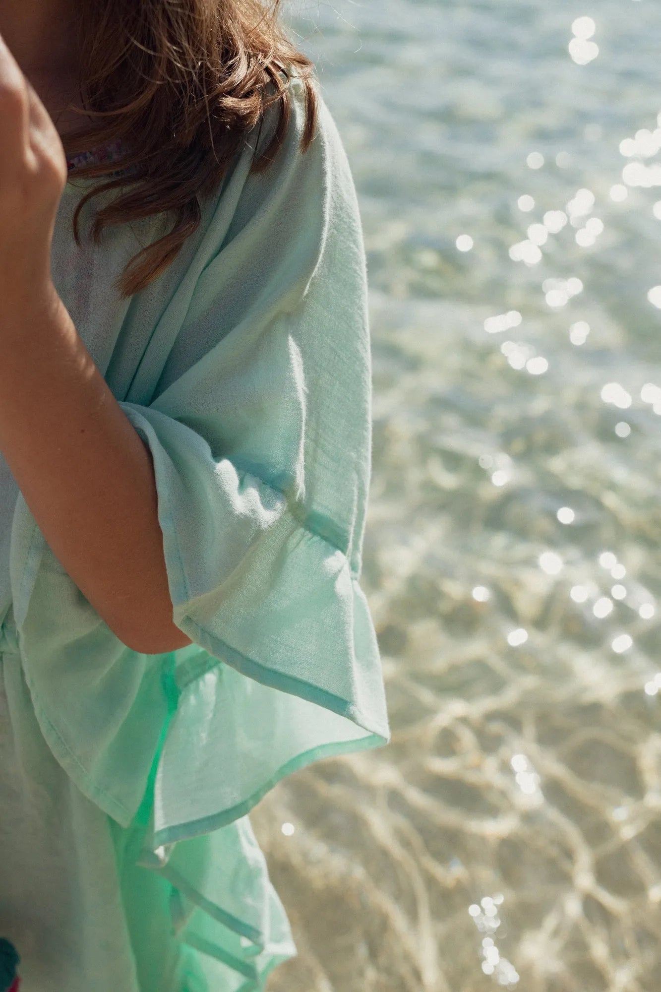 Close-up of girl wearing aqua caftan with pompons by the sparkling water shore