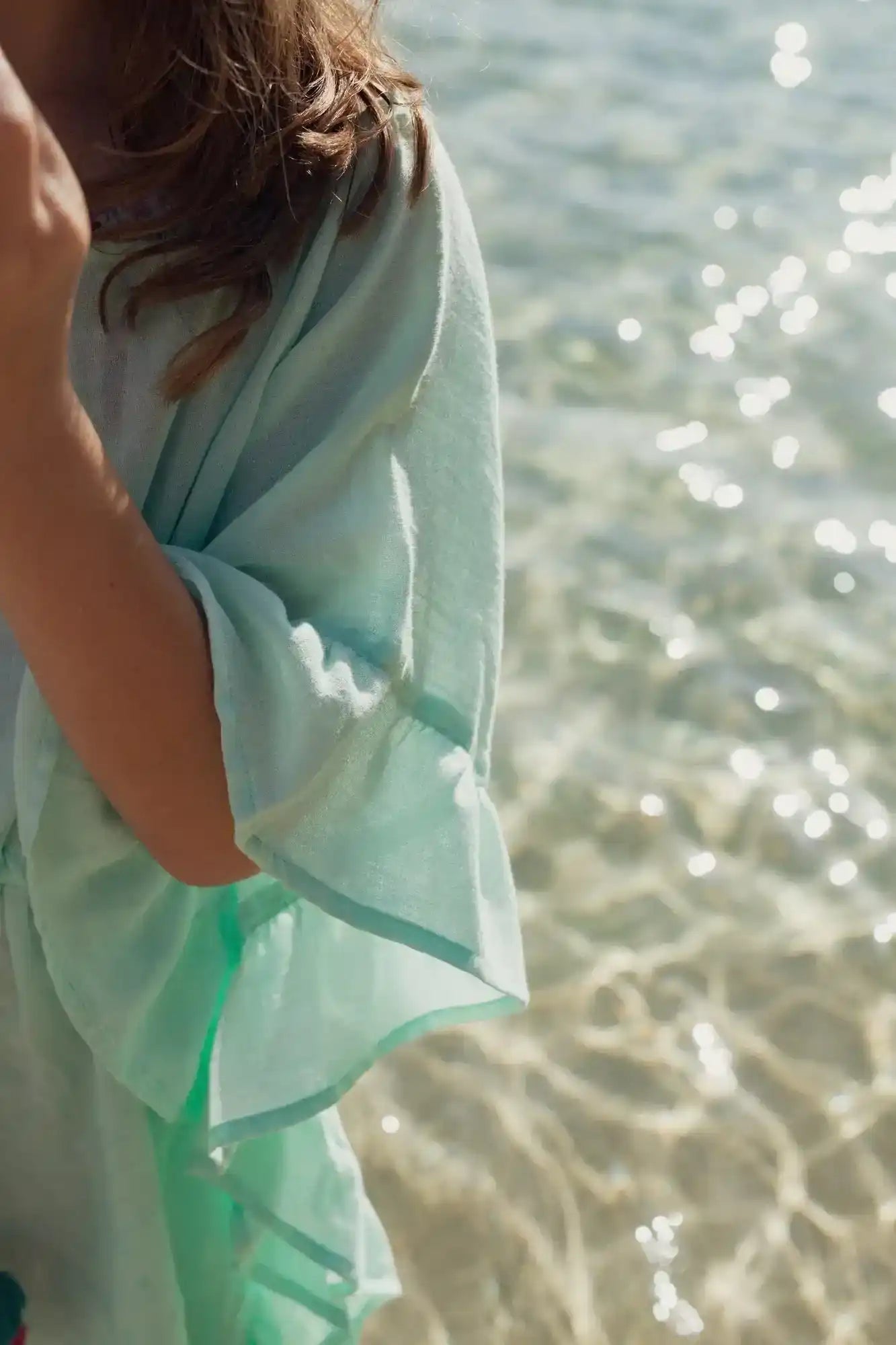 Girl wearing aqua caftan with pom poms by the seaside, beachwear in sunlight