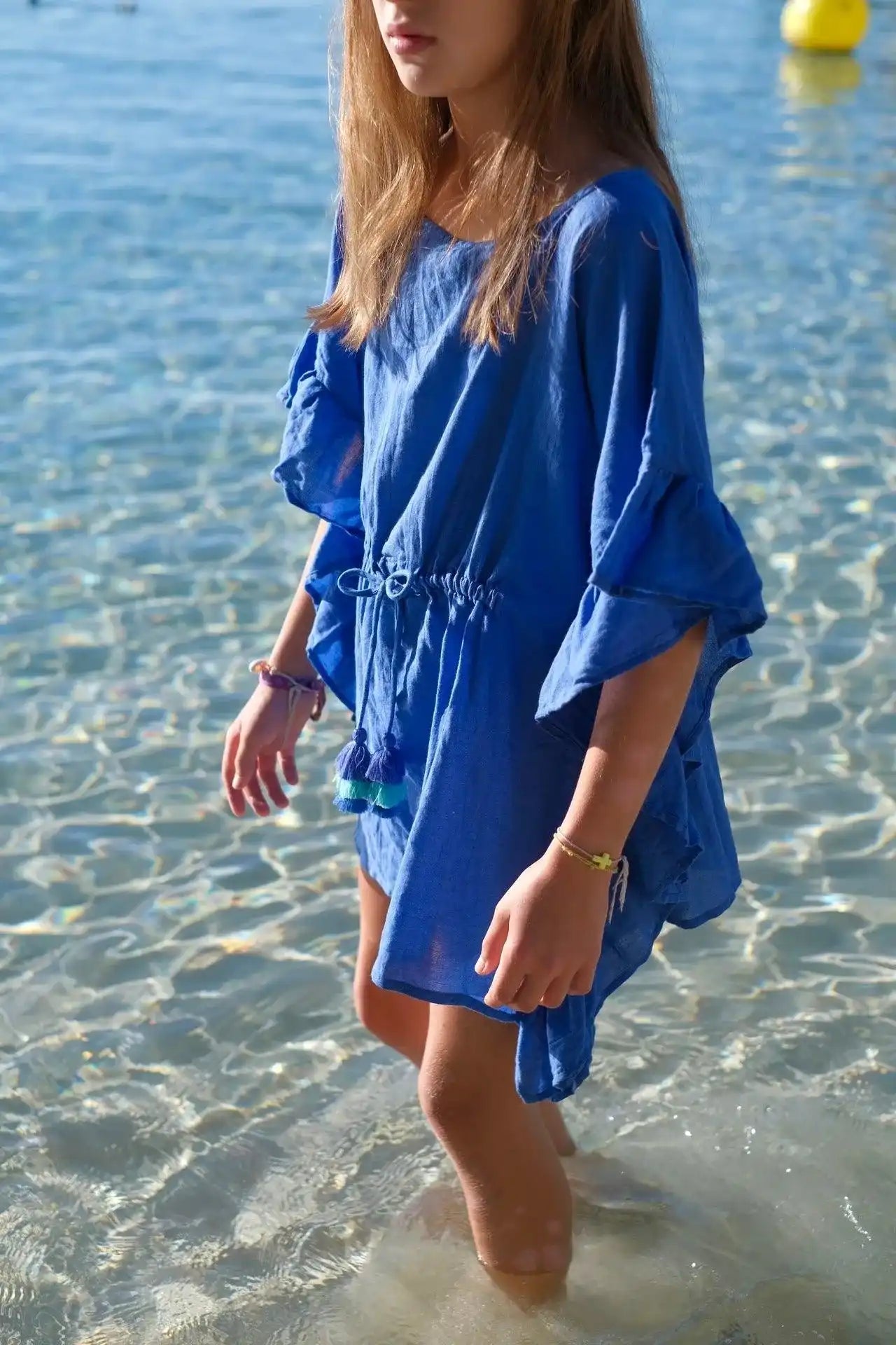 Girl in Lison Paris blue caftan with pompons standing in clear beach water