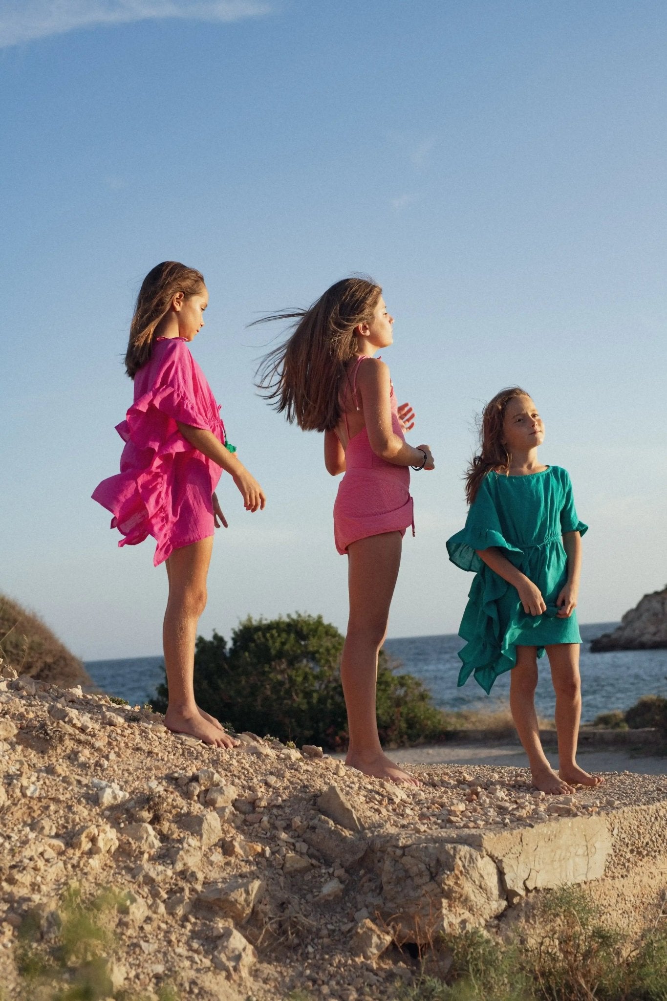 Girls wearing colorful beachwear caftans and swimsuits standing on rocky shore by the sea
