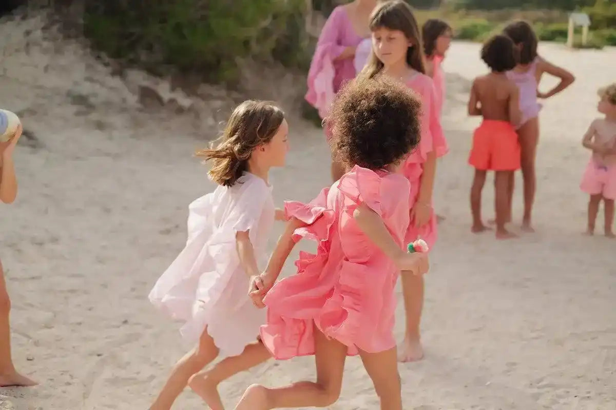 Girls wearing pink and white caftan beachwear playing together on a sandy beach