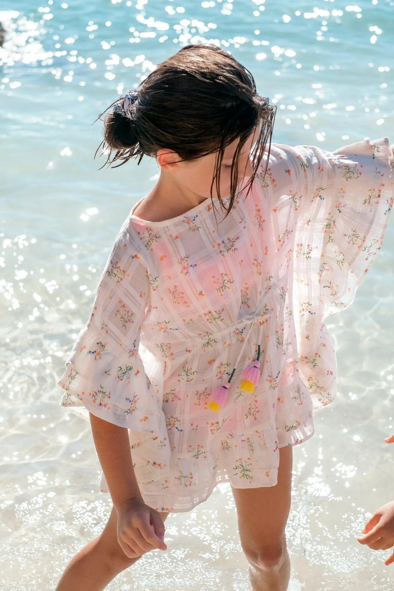 Young girl at the beach wearing a white cotton floral print caftan with tassels