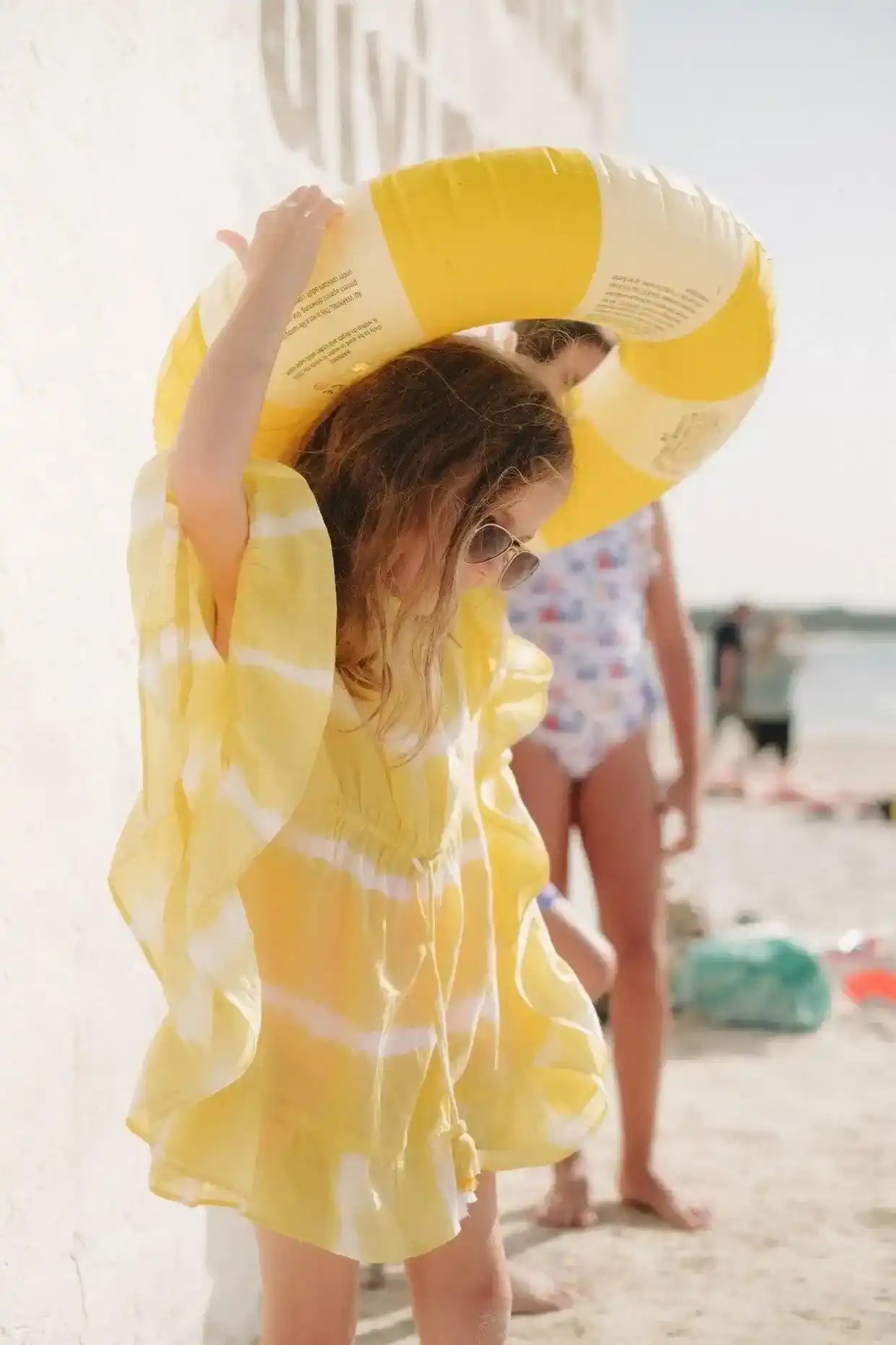 Girl in yellow tie-dye caftan with swim ring at sunny beach