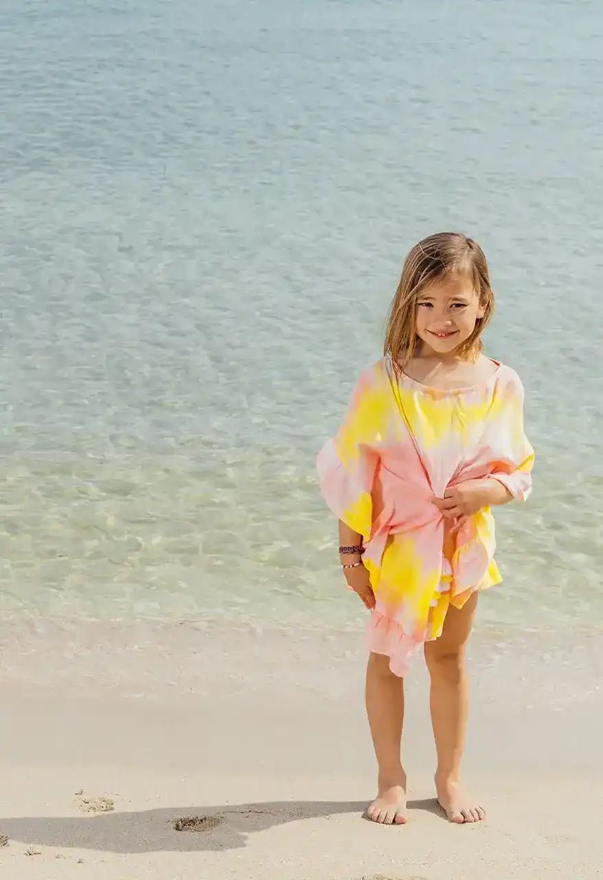 girl in pink and yellow tie-dye caftan standing on the beach by the sea