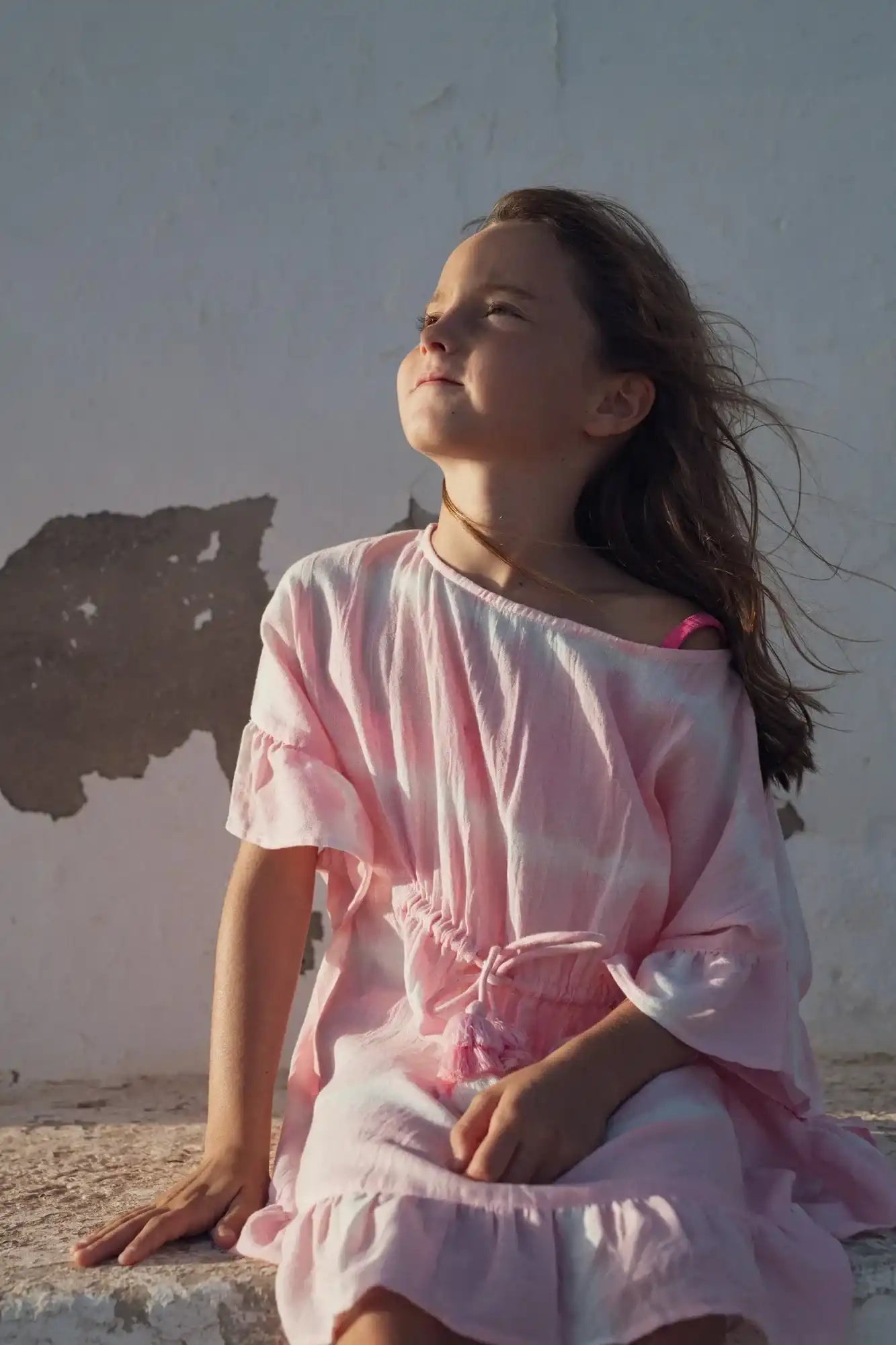Girl wearing pink tie-dye caftan dress, sitting outdoors in sunlight, Lison Paris beachwear