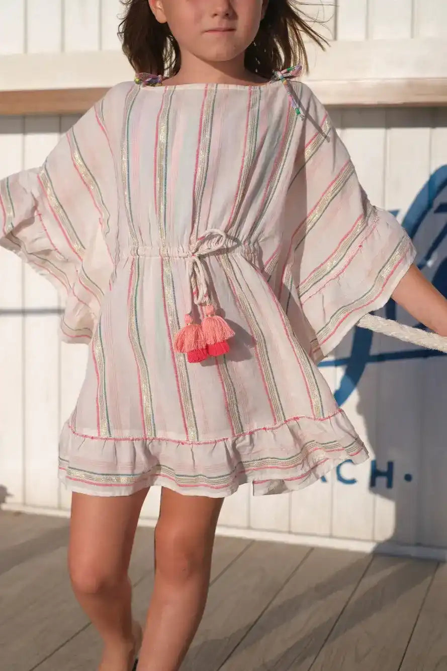 Girl wearing pink and gold striped caftan dress with tassels, standing outdoors