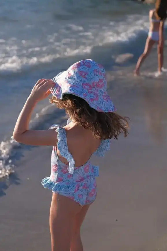 Girl in blue floral swimsuit and sun hat by the sea, Lison Paris beachwear collection