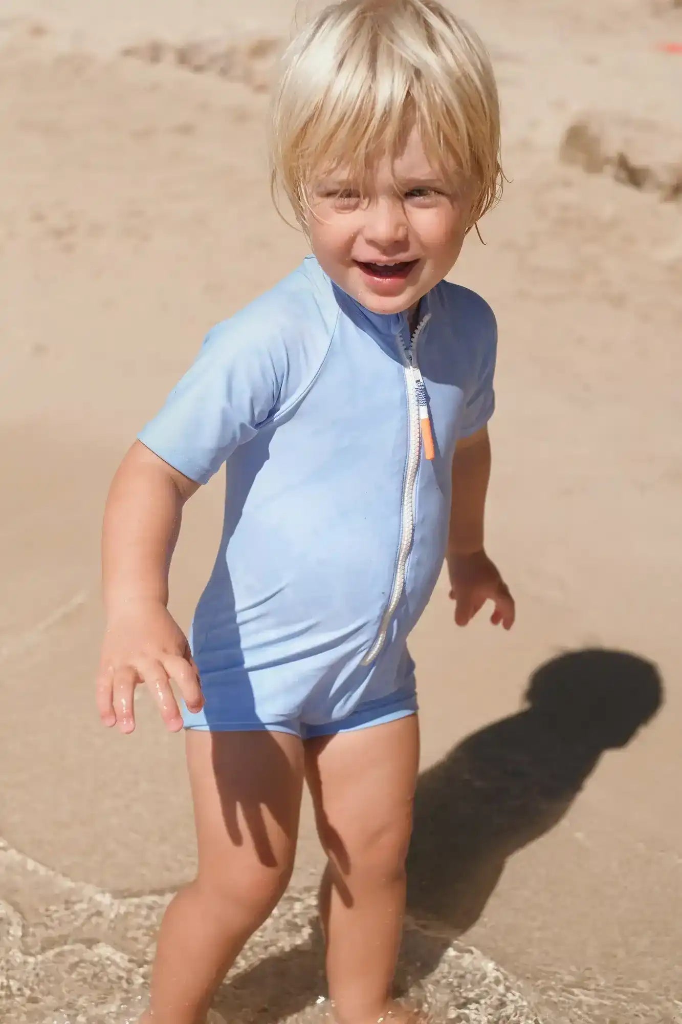 Little boy in light blue short-sleeve UV swimsuit playing on the beach