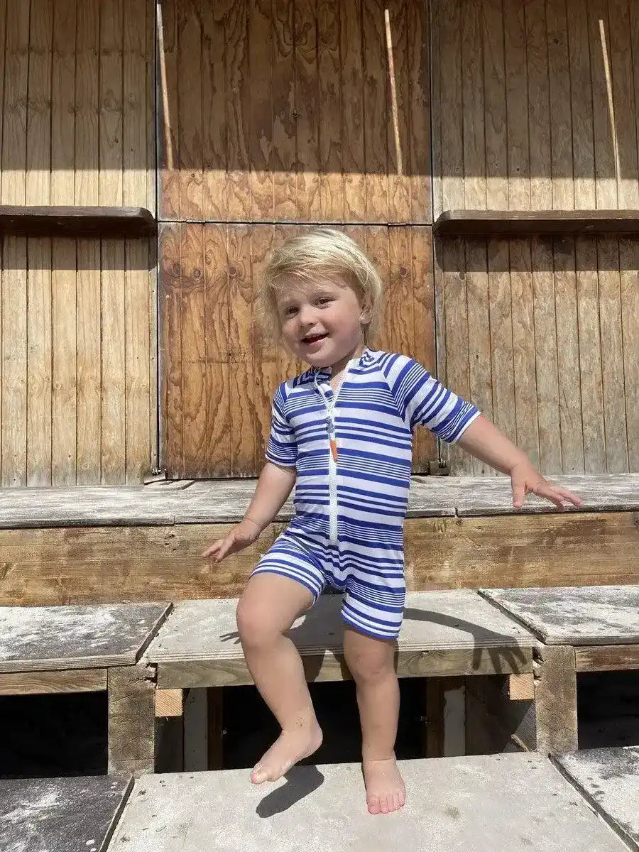 Young boy in a blue and white striped short-sleeve UV swim romper outdoors