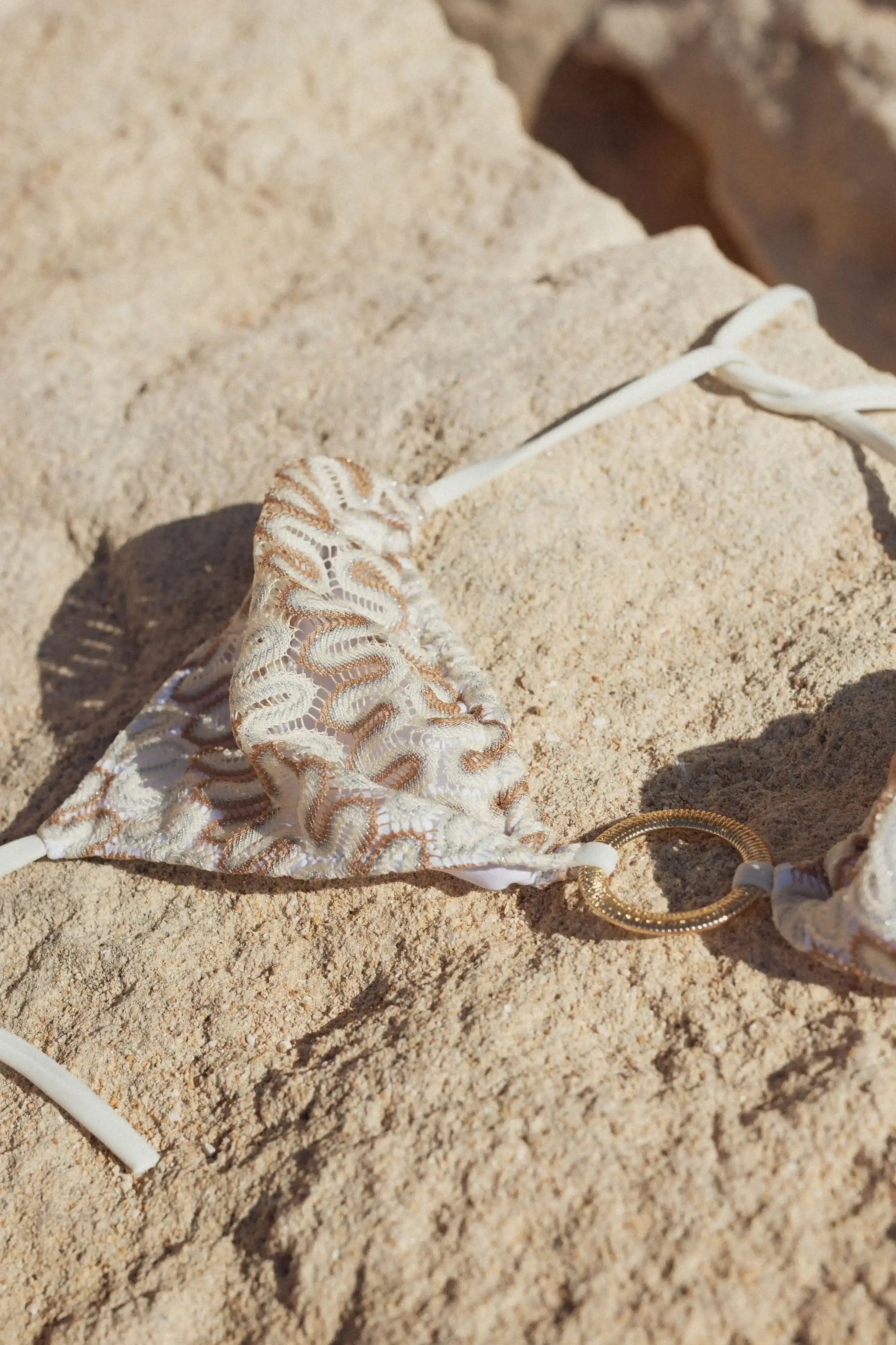 White crochet bikini top with gold ring detail on sandy rock background