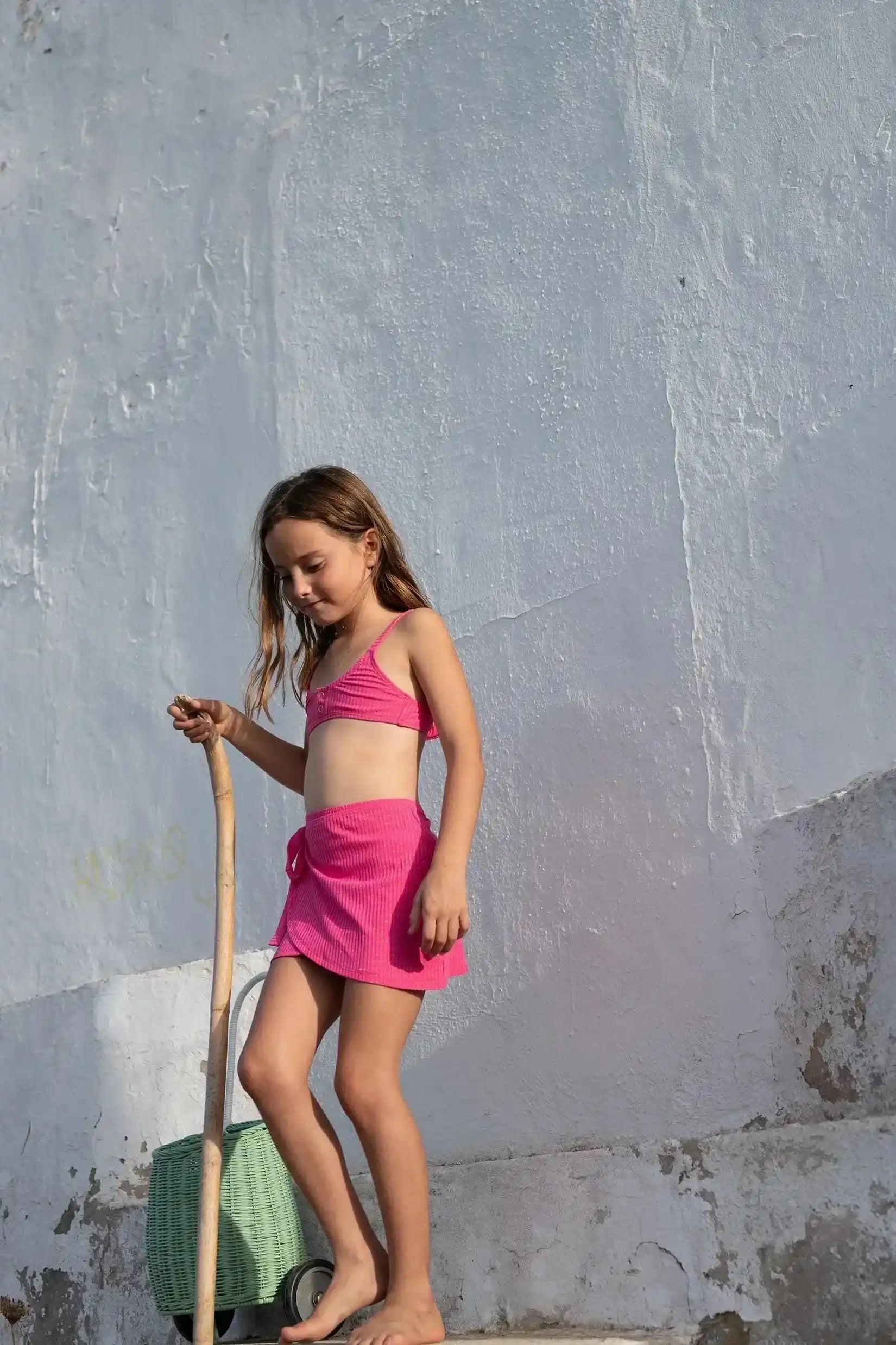 Girl in pink two-piece swimsuit and wrap skirt walking outdoors, summer beachwear Lison Paris