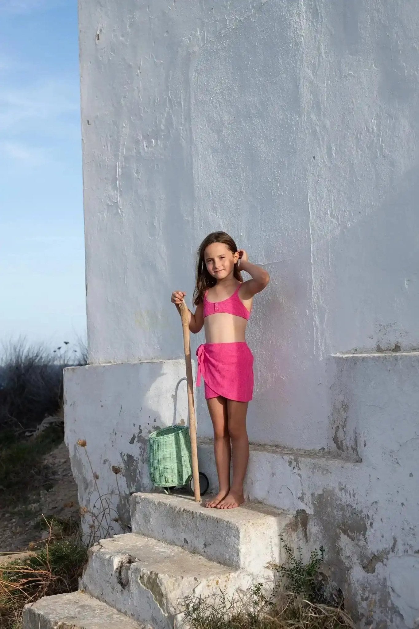 Girl in pink knotted skirt and swim top standing outdoors on stone steps