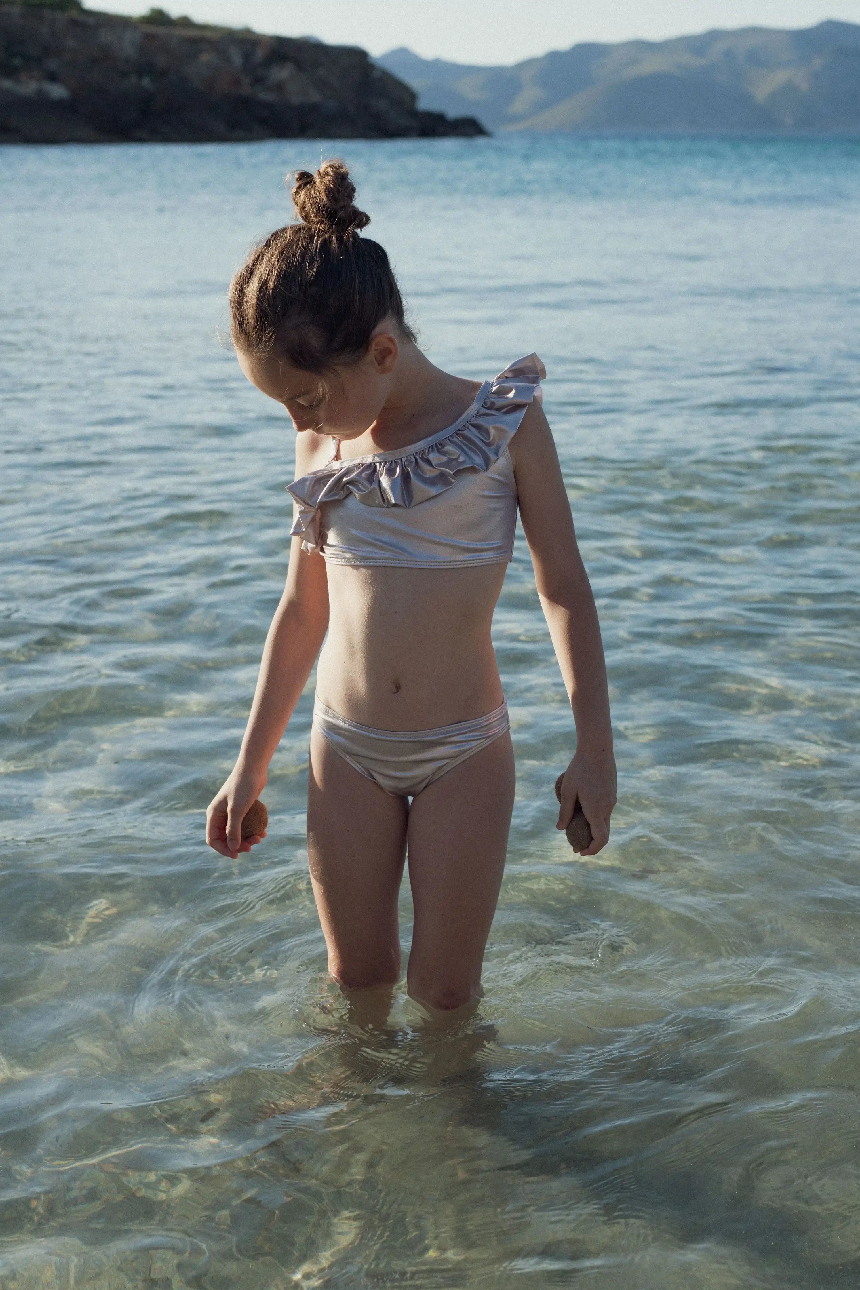 Girl in iridescent gold asymmetric swimsuit standing in clear water, Lison Paris beachwear