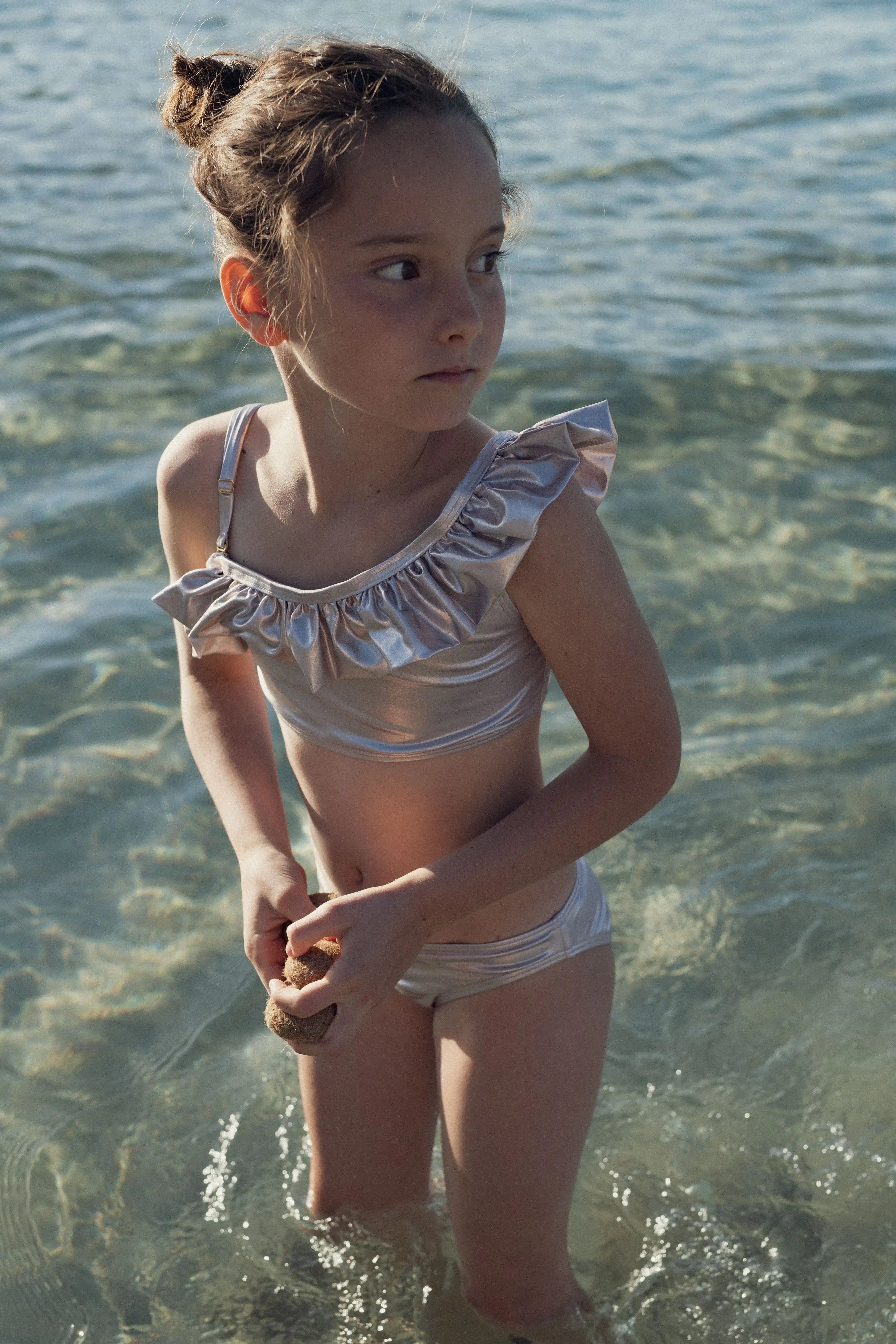 Girl wearing iridescent champagne asymmetrical swimsuit by Lison Paris in the sea