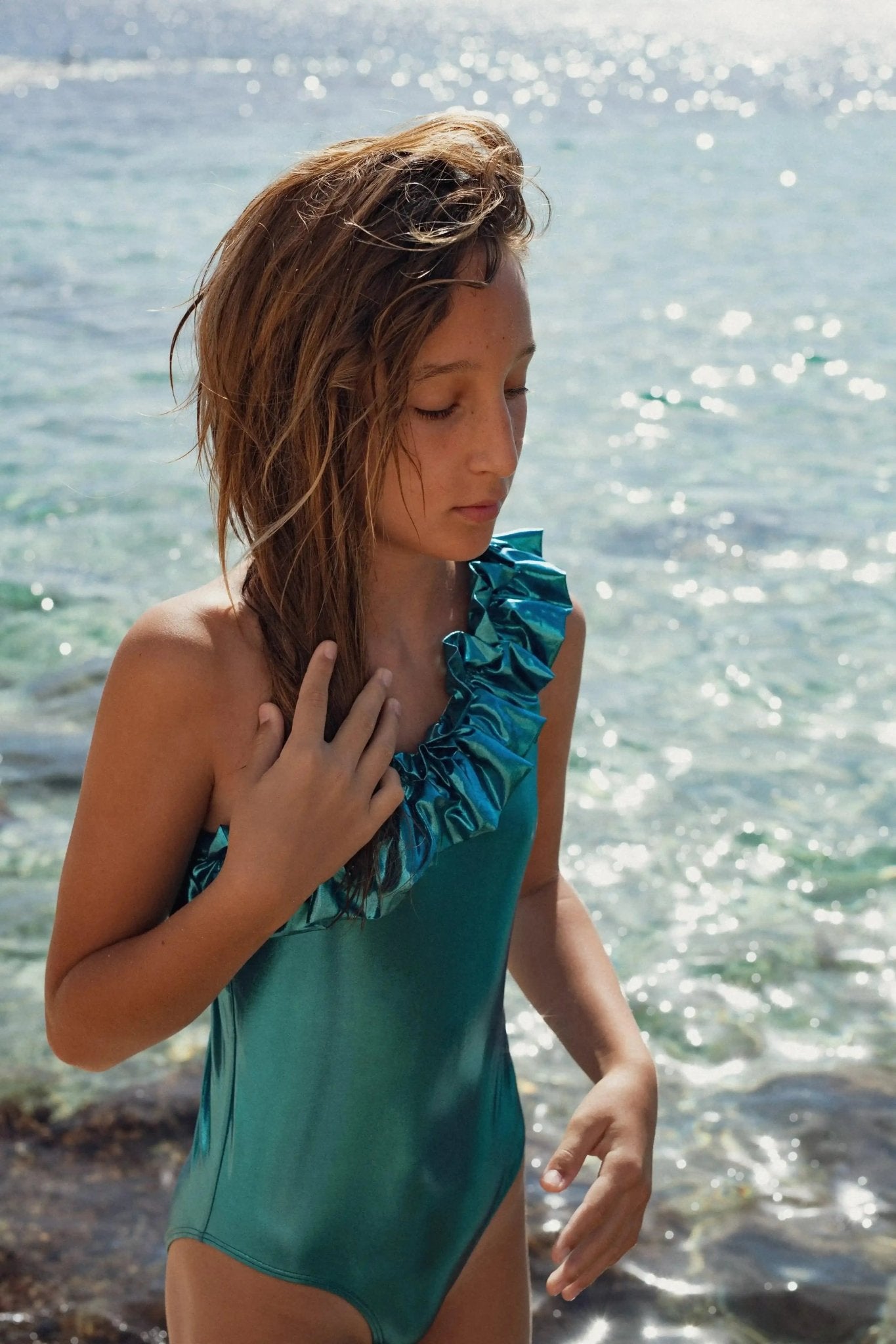Girl wearing asymmetrical emerald iridescent one-piece swimsuit by the sea