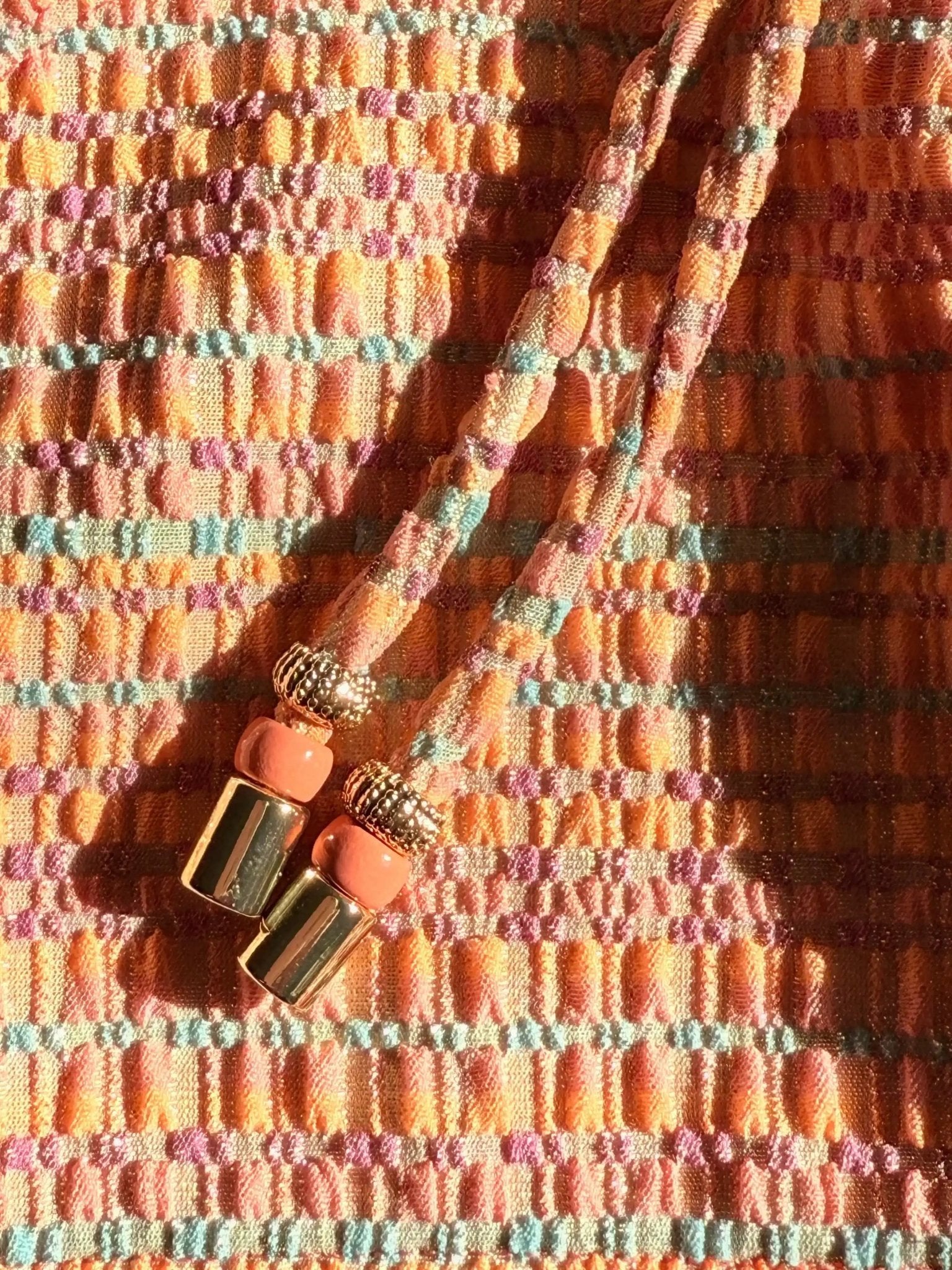 Close-up of textured coral and gold two-piece swimsuit fabric with decorative ties