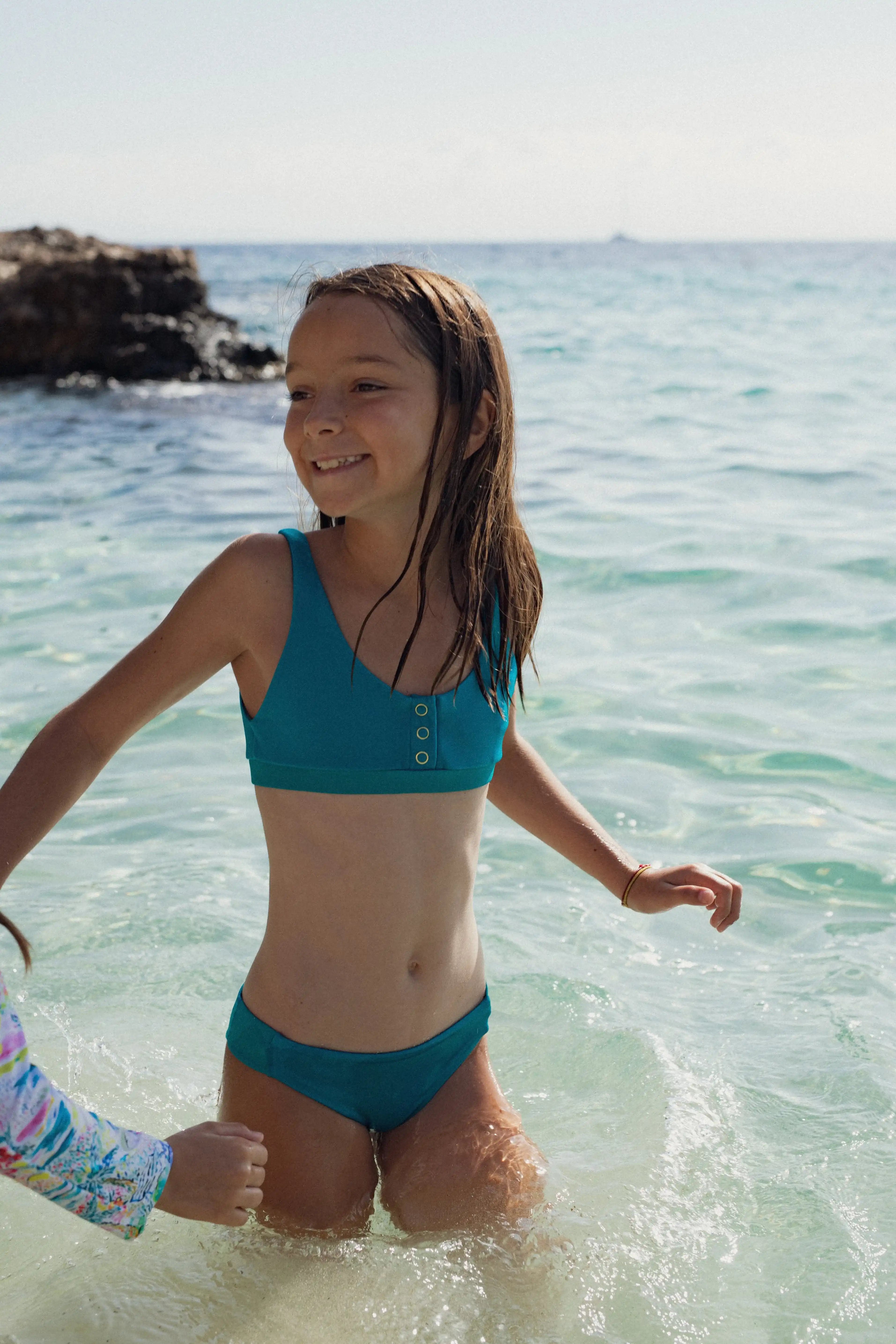 Girl wearing Lison Paris anti-UV teal two-piece swimsuit smiling in the sea