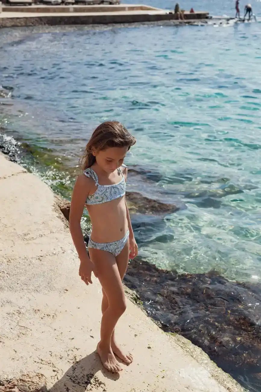 Girl in blue two-piece swimsuit standing by the sea on a sunny beach day