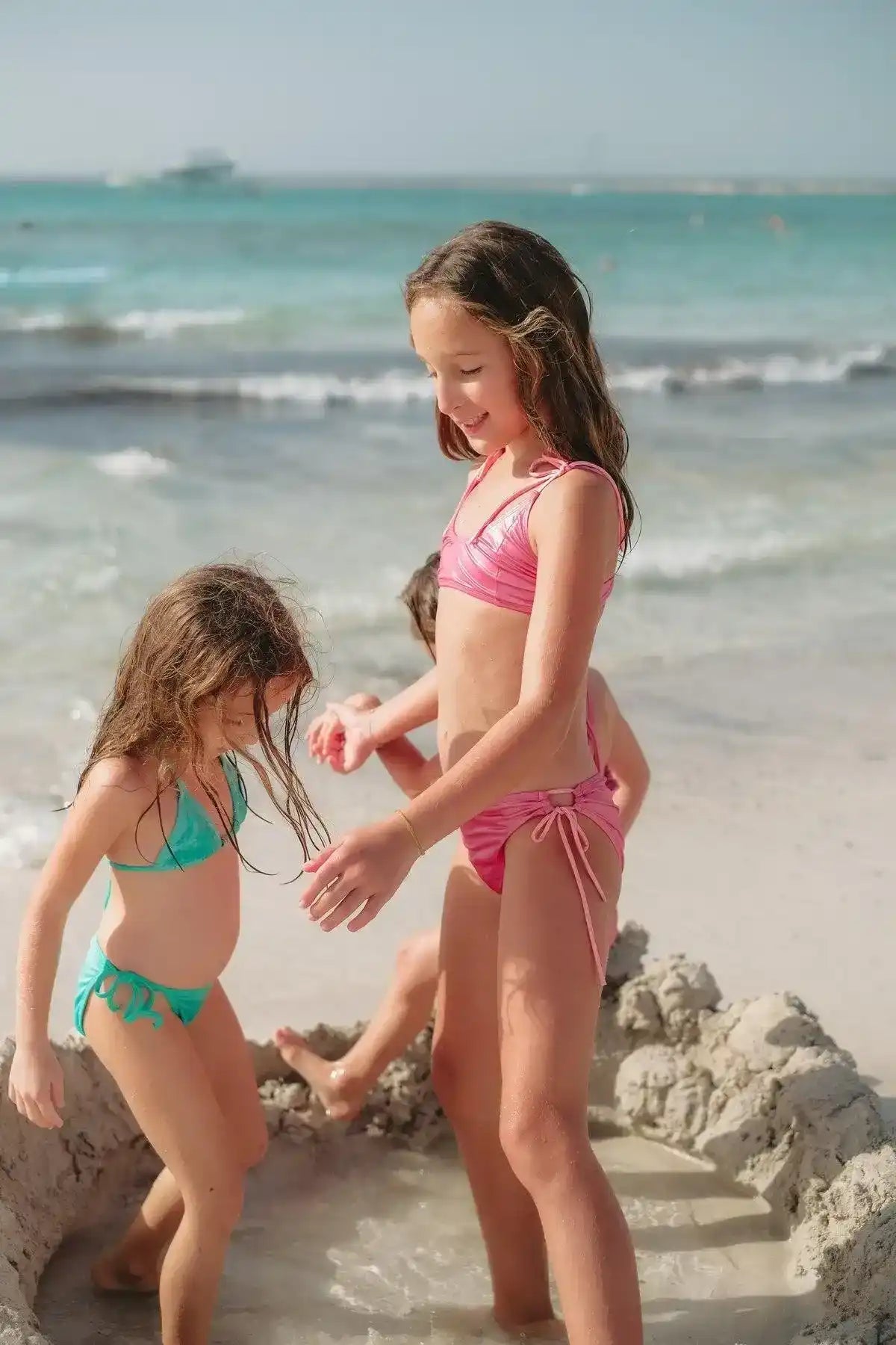Girls in iridescent two-piece swimsuits playing on sandy beach by the sea