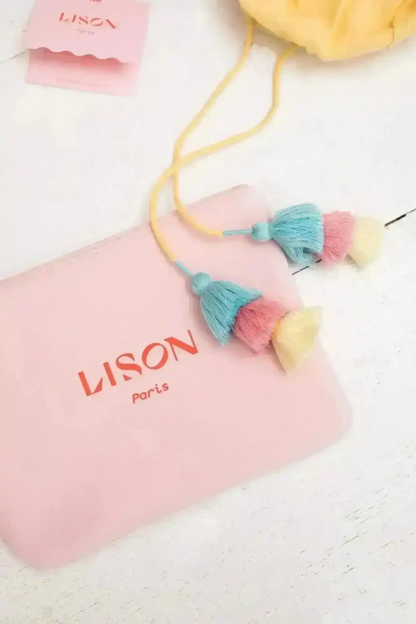 Lison Paris pink pouch with logo and pastel tassels, beachwear accessories flat lay