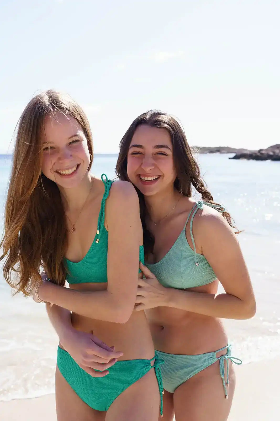 Two girls in green textured bikinis smiling on a sunny beach