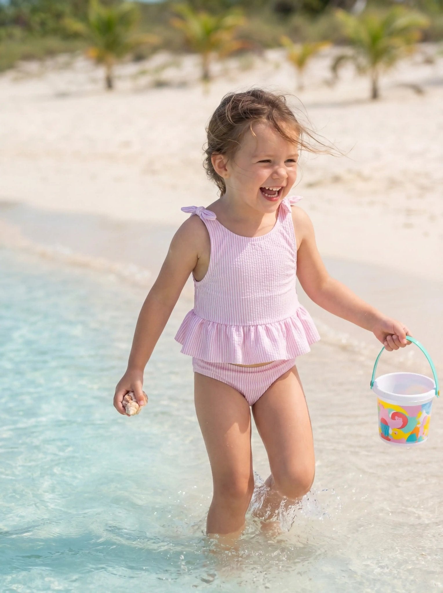Young girl in lilac striped two-piece swimsuit playing on the beach near water