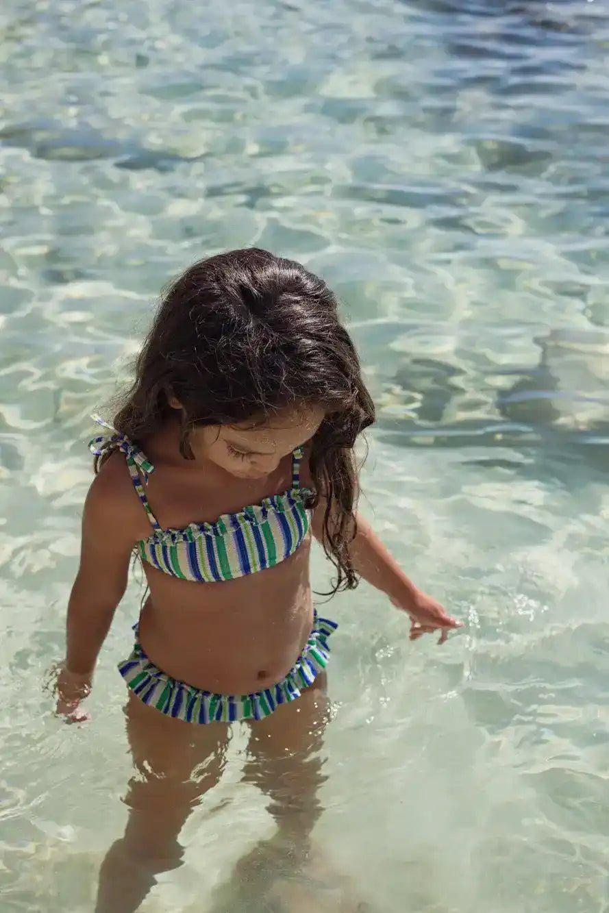 Girl wearing blue and green striped two-piece swimsuit standing in clear water