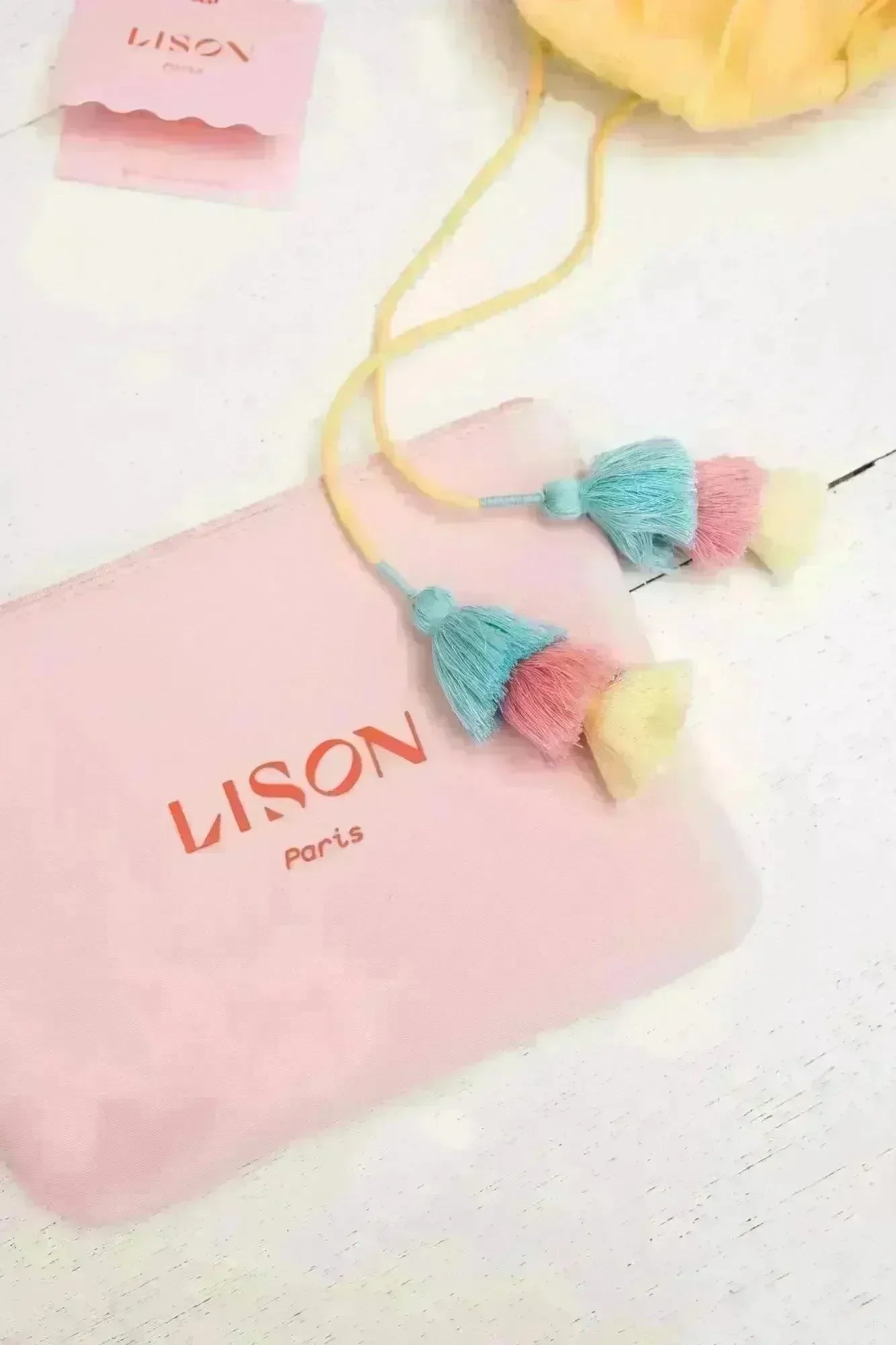 Pink Lison Paris pouch with multicolor tassel strings on white wooden surface